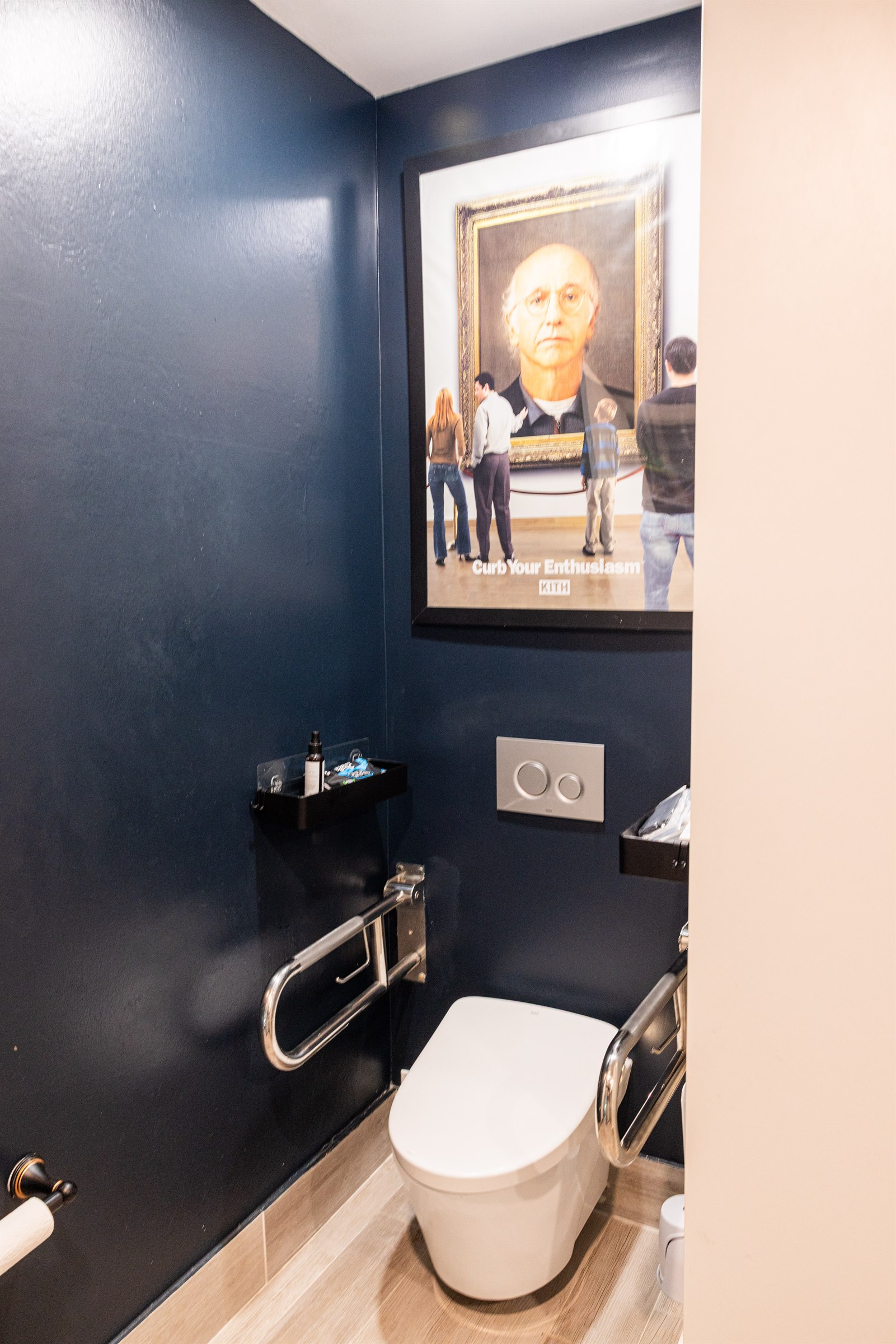 Navy powder room with a comfort-height toilet, fold-down grab bar, and framed artwork
