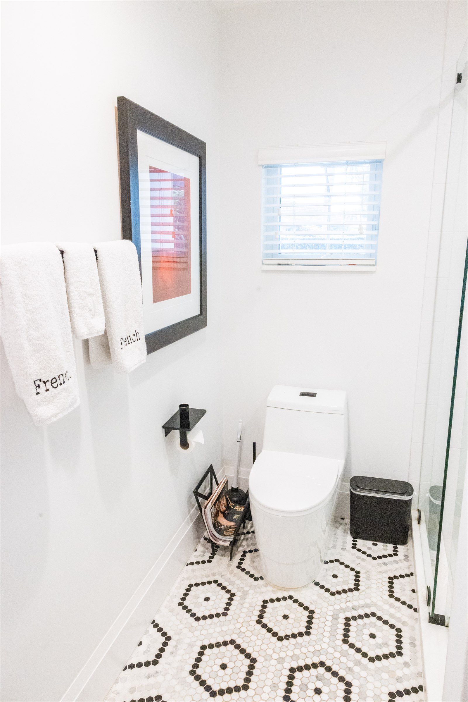 Guest powder room with monogrammed towels, black-framed art, and hexagon tile floor