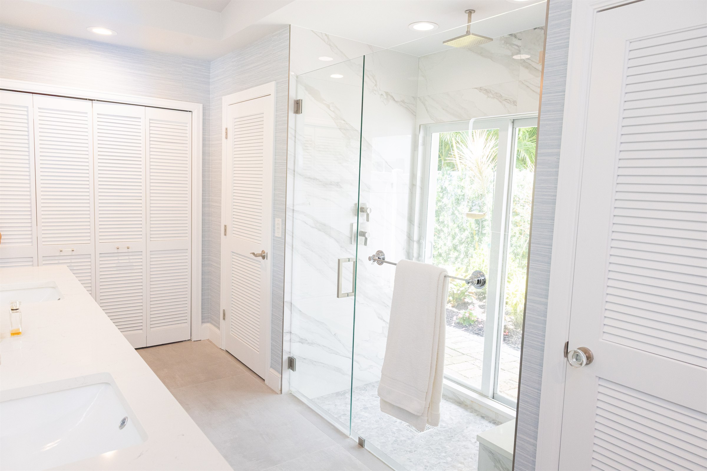 Louvered closet doors beside a marble shower with garden views