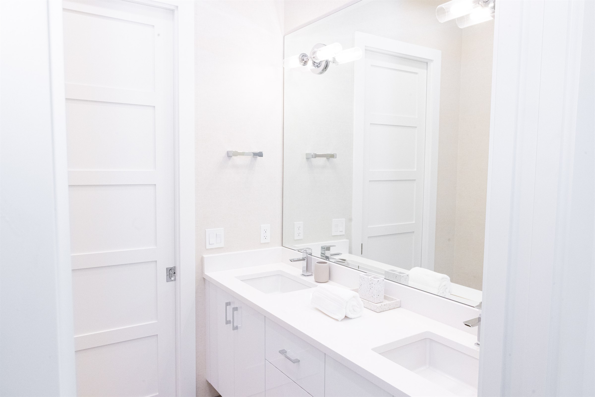 Simple white double vanity guest bath with chrome fixtures and a pocket door