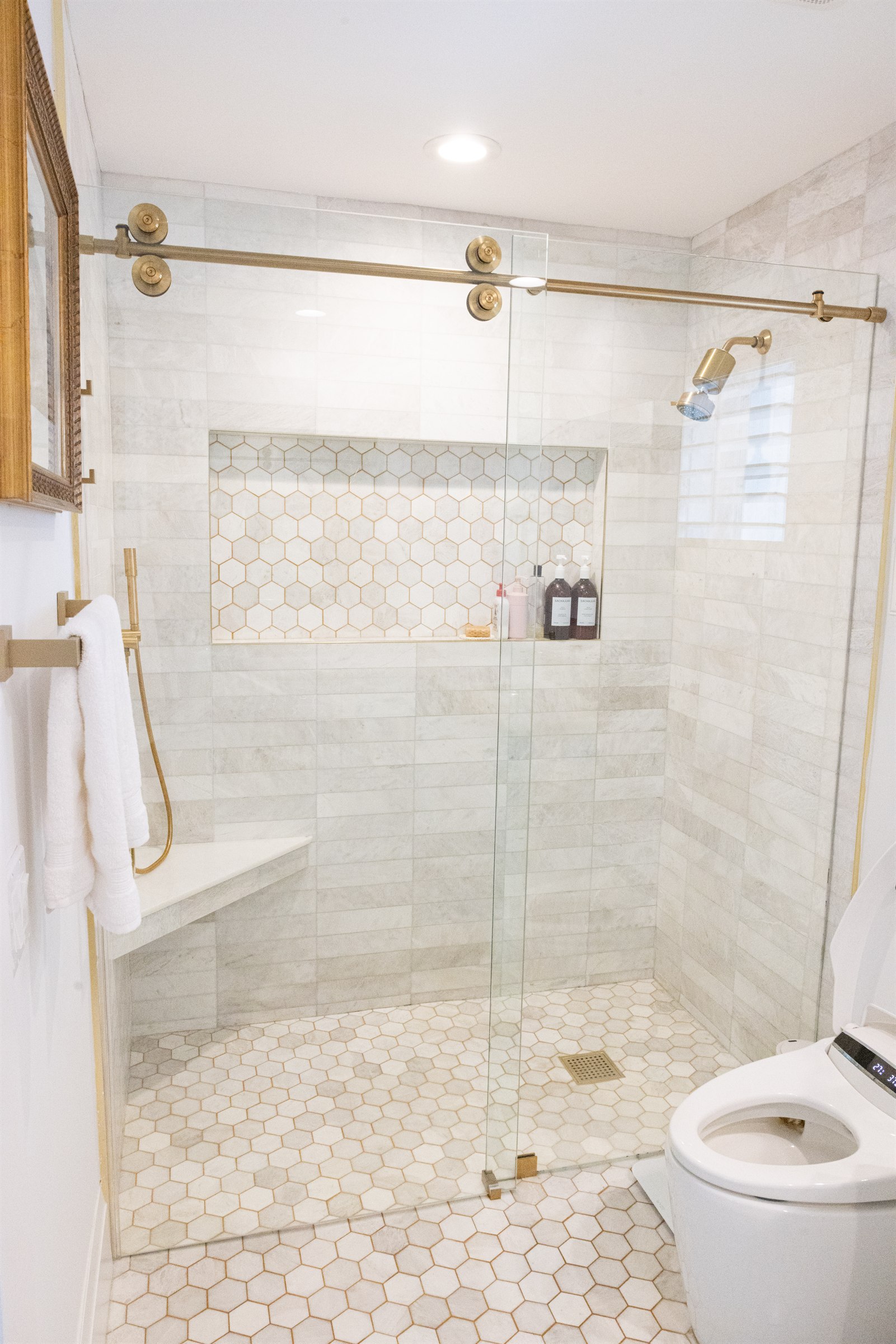 Walk-in shower with marble subway tile, hexagonal mosaic niche, and brushed gold hardware
