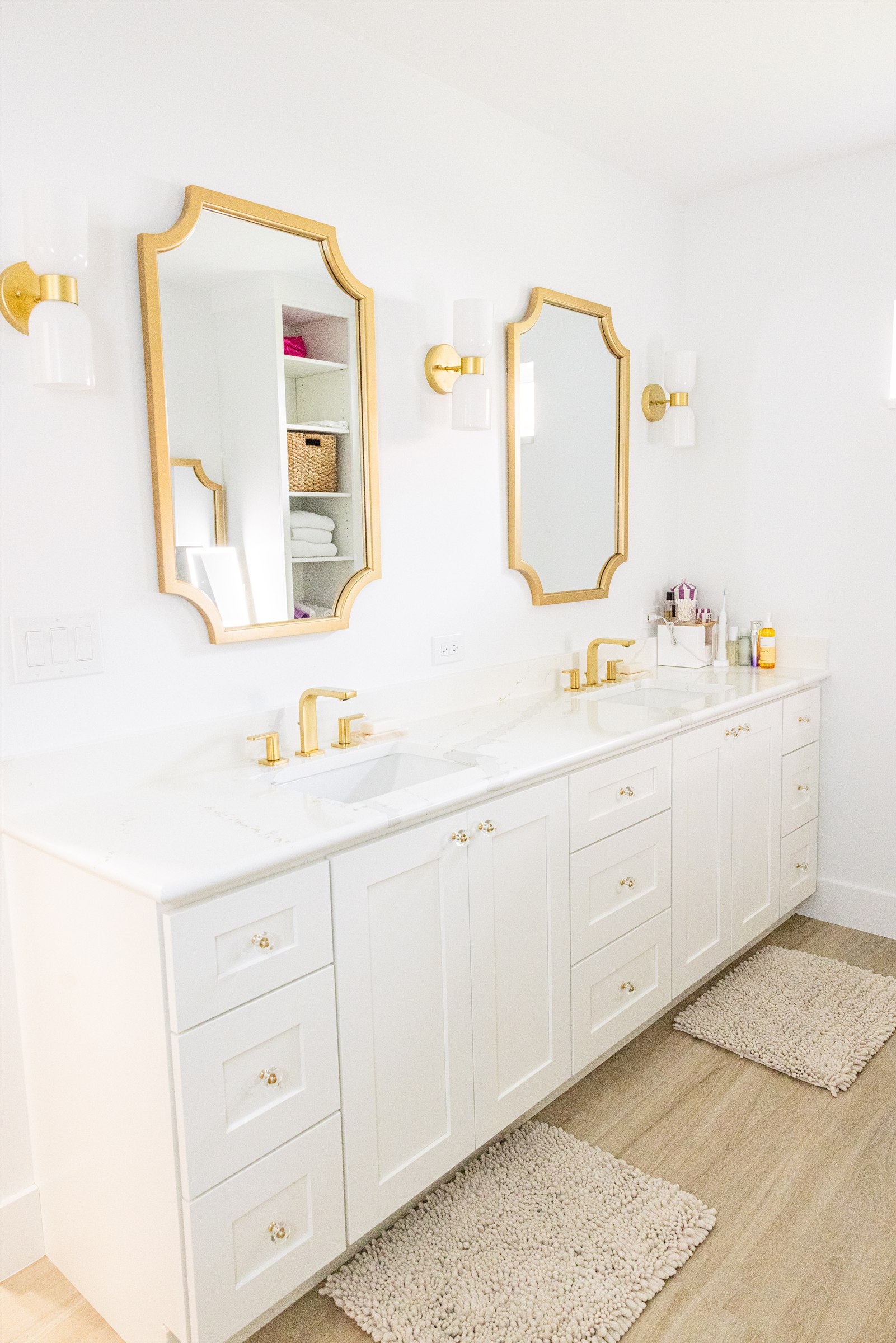 Double vanity with tall gold rectangular mirrors and folded linen closet beyond