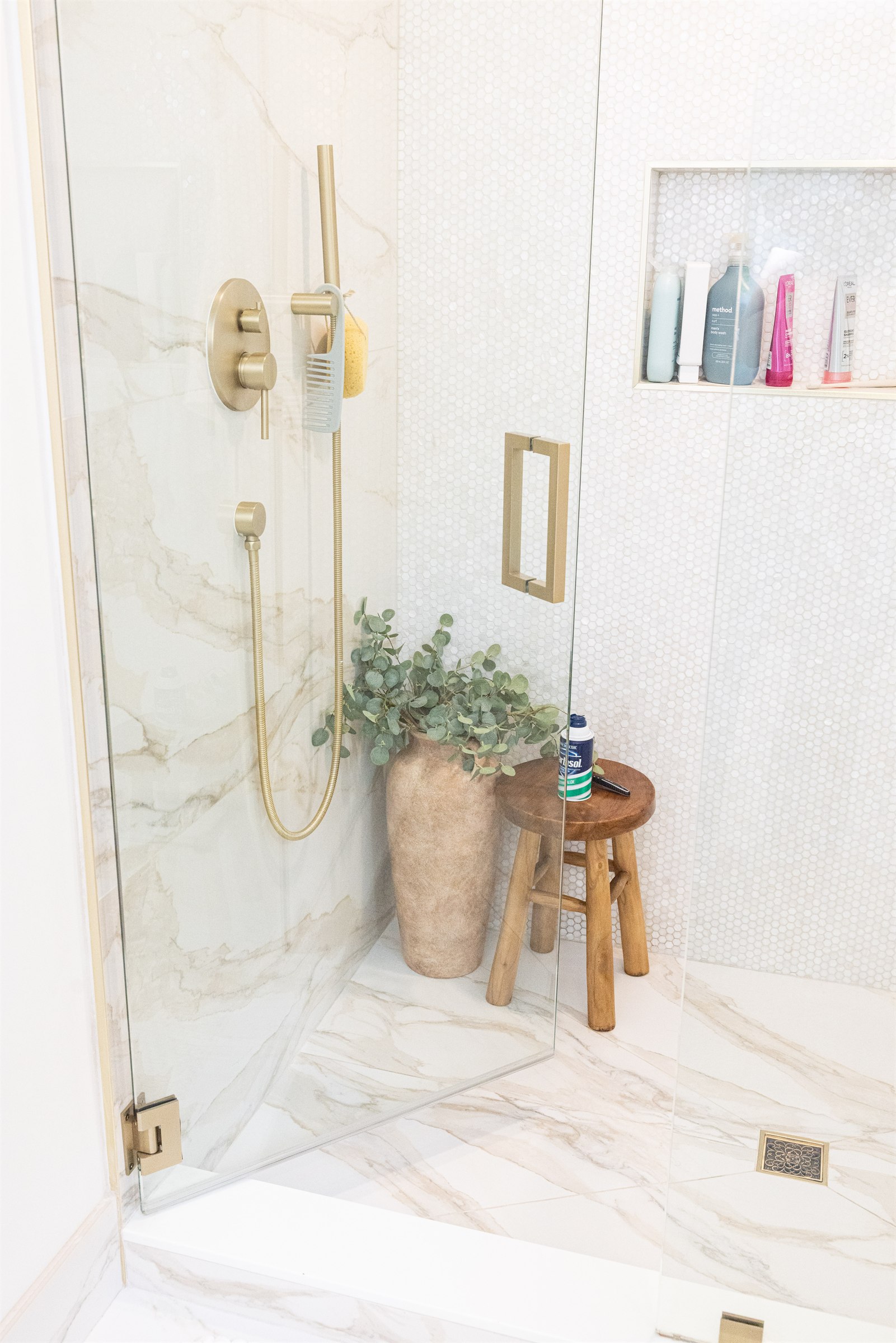 Walk-in shower corner with teak stool, eucalyptus, and brushed gold fixtures