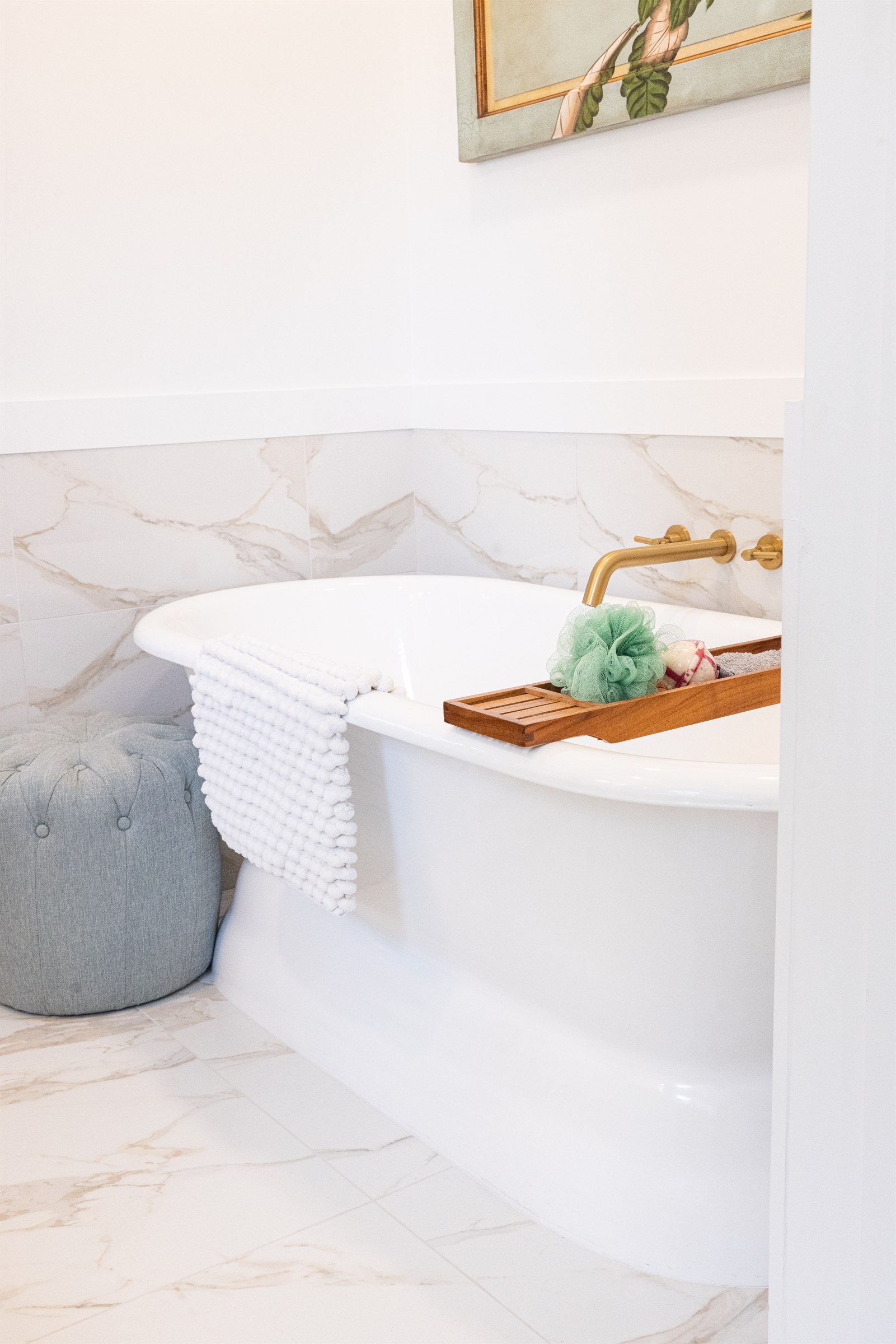 Freestanding soaking tub with wood caddy, loofah, and marble tile surround