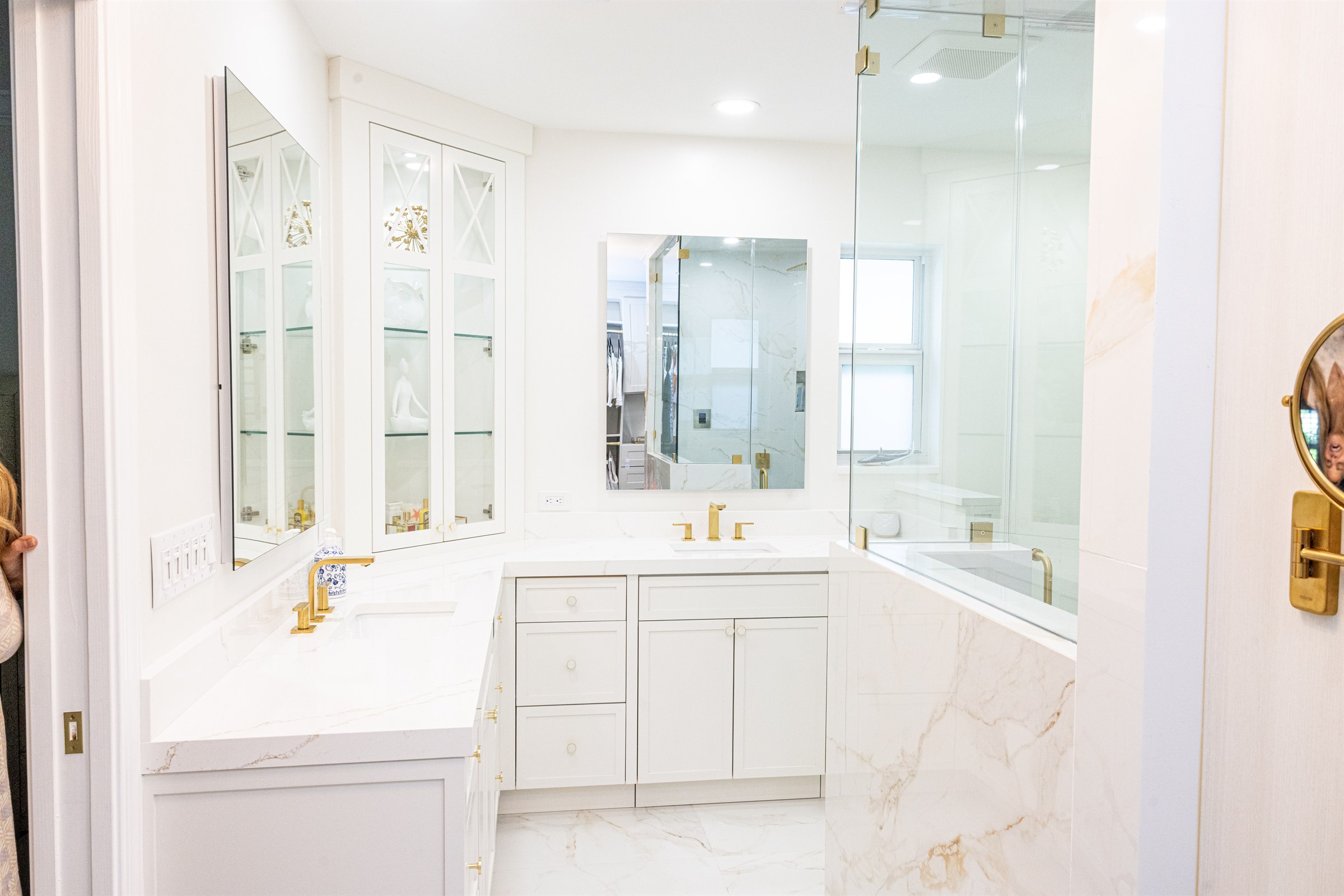 Vanity nook with gold sconces and a mirror reflecting the marble shower