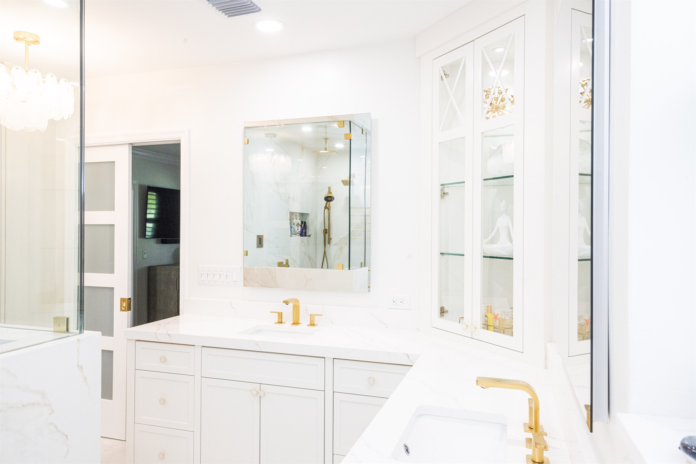 Vanity with glass display cabinets, marble shower reflection, and closet television