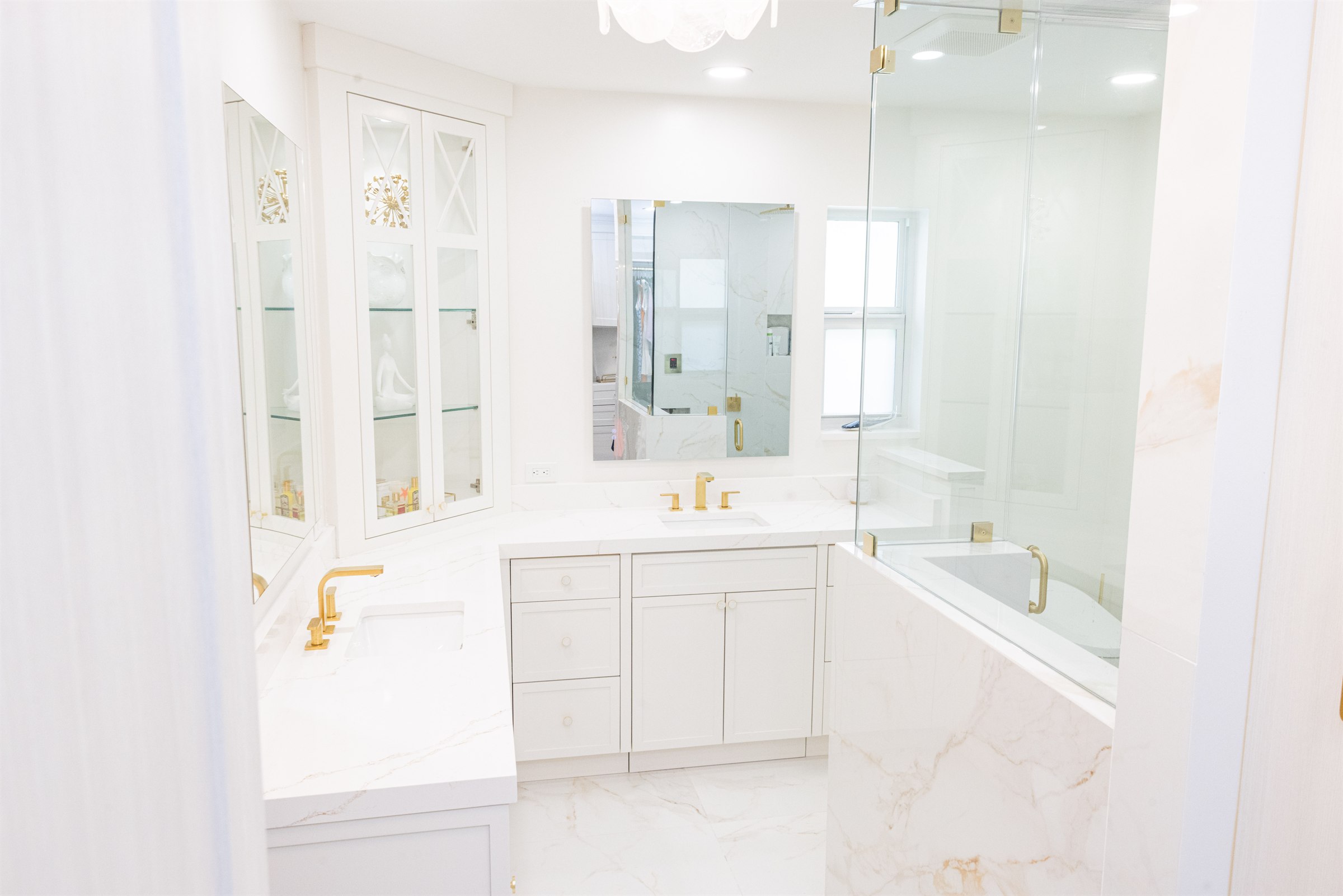 Corner vanity with glass cabinetry, marble tub surround, and walk-in shower
