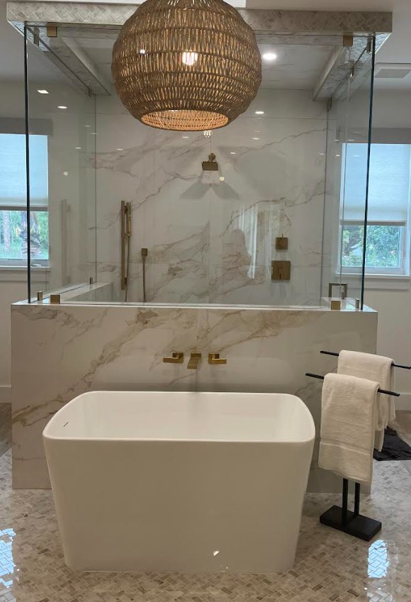 Freestanding tub beside a marble walk-in shower beneath a woven pendant light