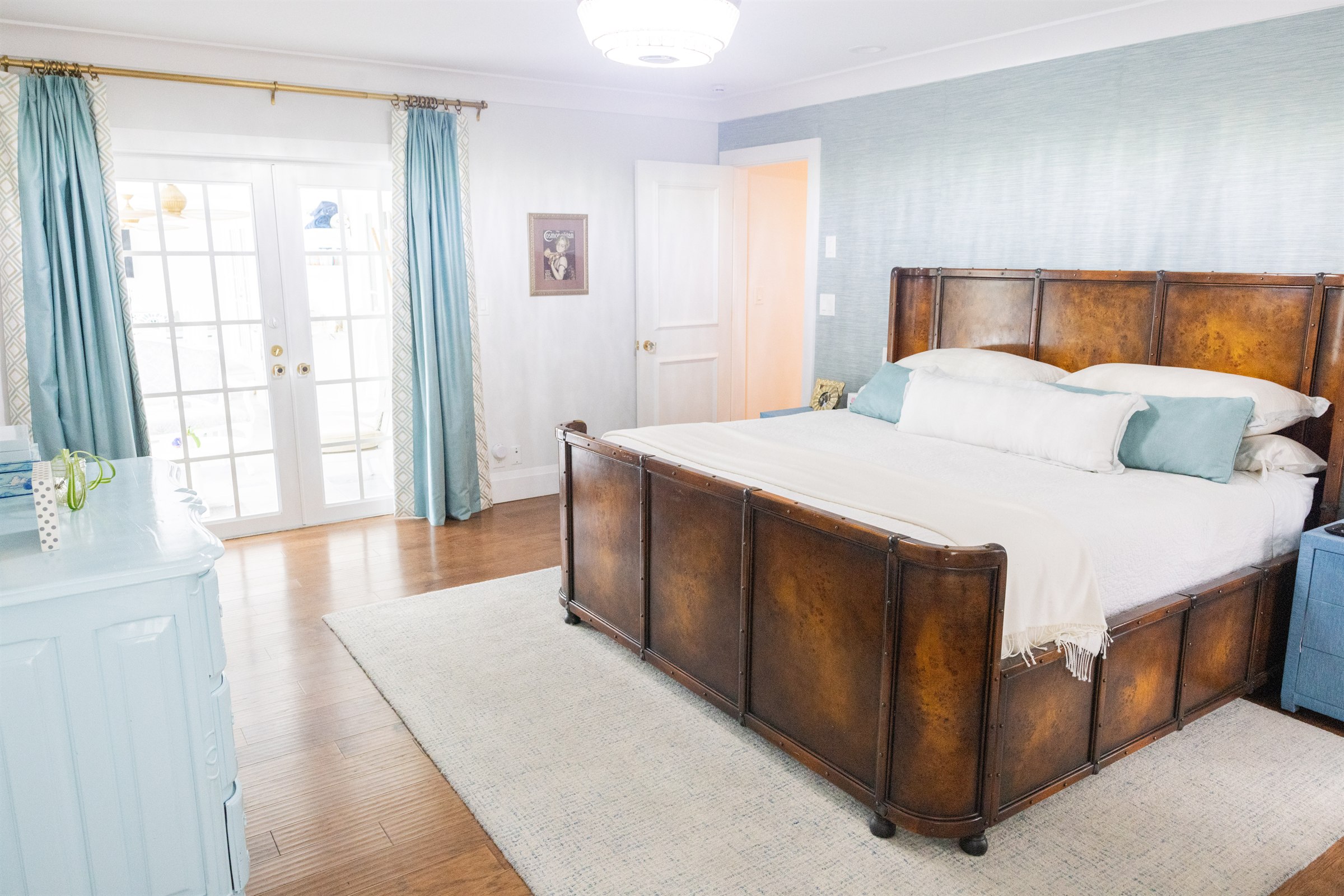 Bedroom with tufted leather panel bed, teal grasscloth accent wall, and French doors