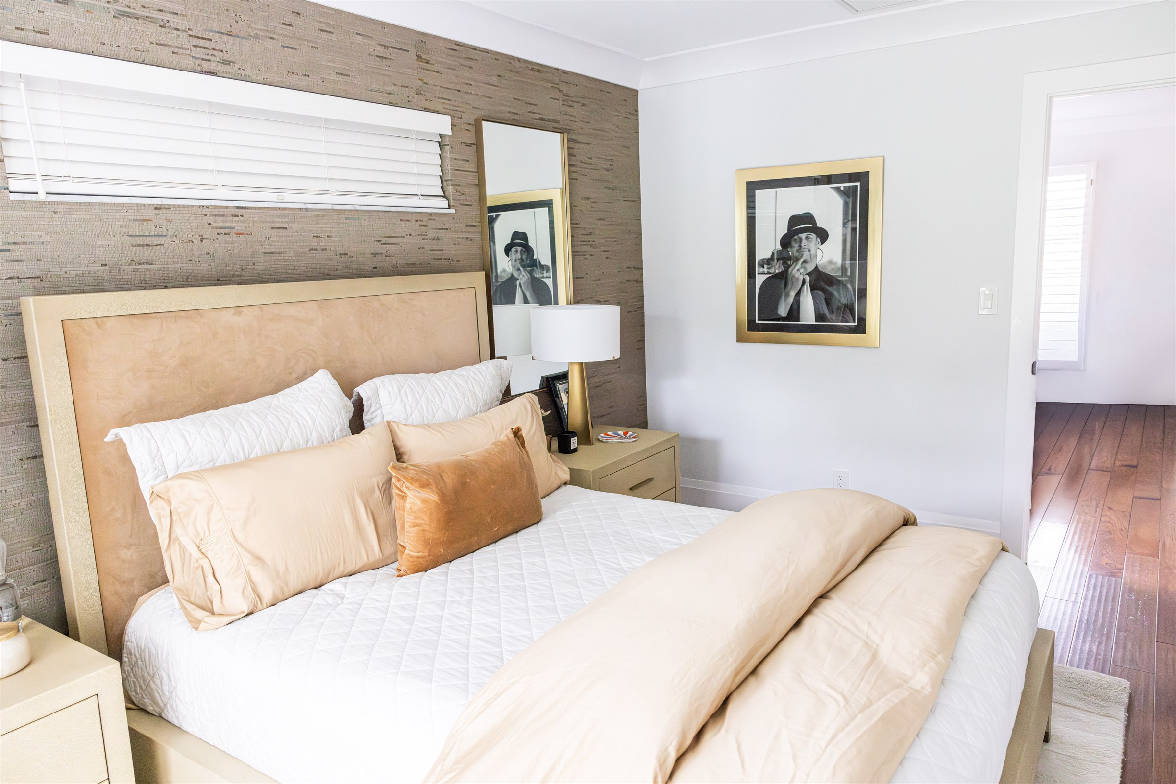 Bedroom with gold velvet headboard, grasscloth wall, and framed black-and-white portrait