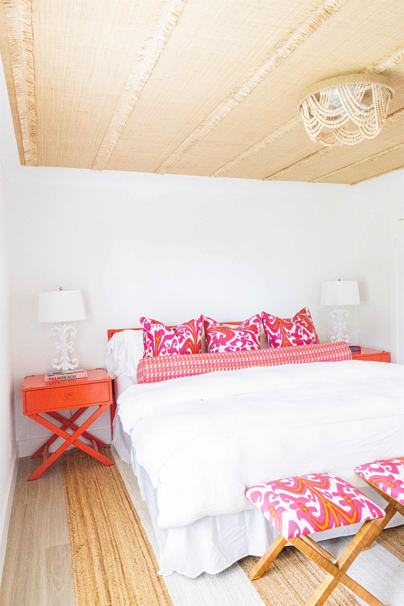 Bright guest bedroom with raffia ceiling, coral ikat bedding, and beaded chandelier