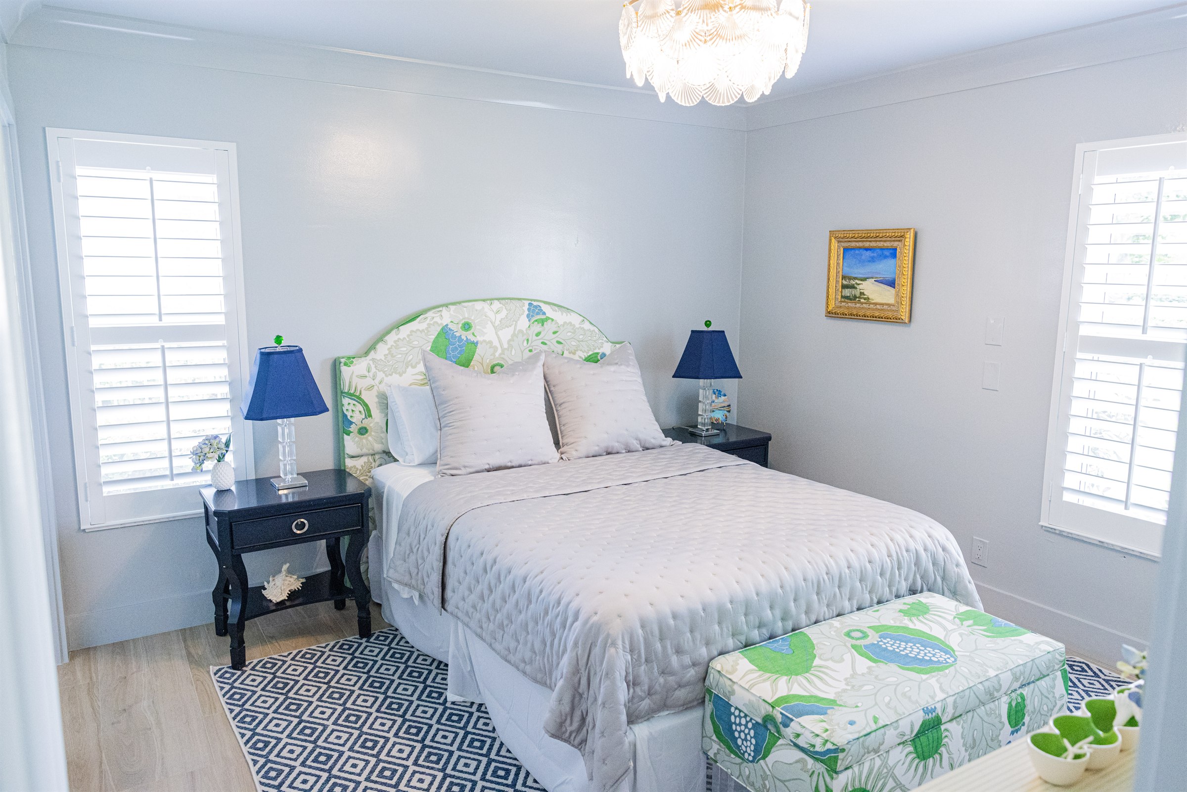 Guest bedroom with green and blue floral headboard, navy nightstands, and diamond-pattern rug