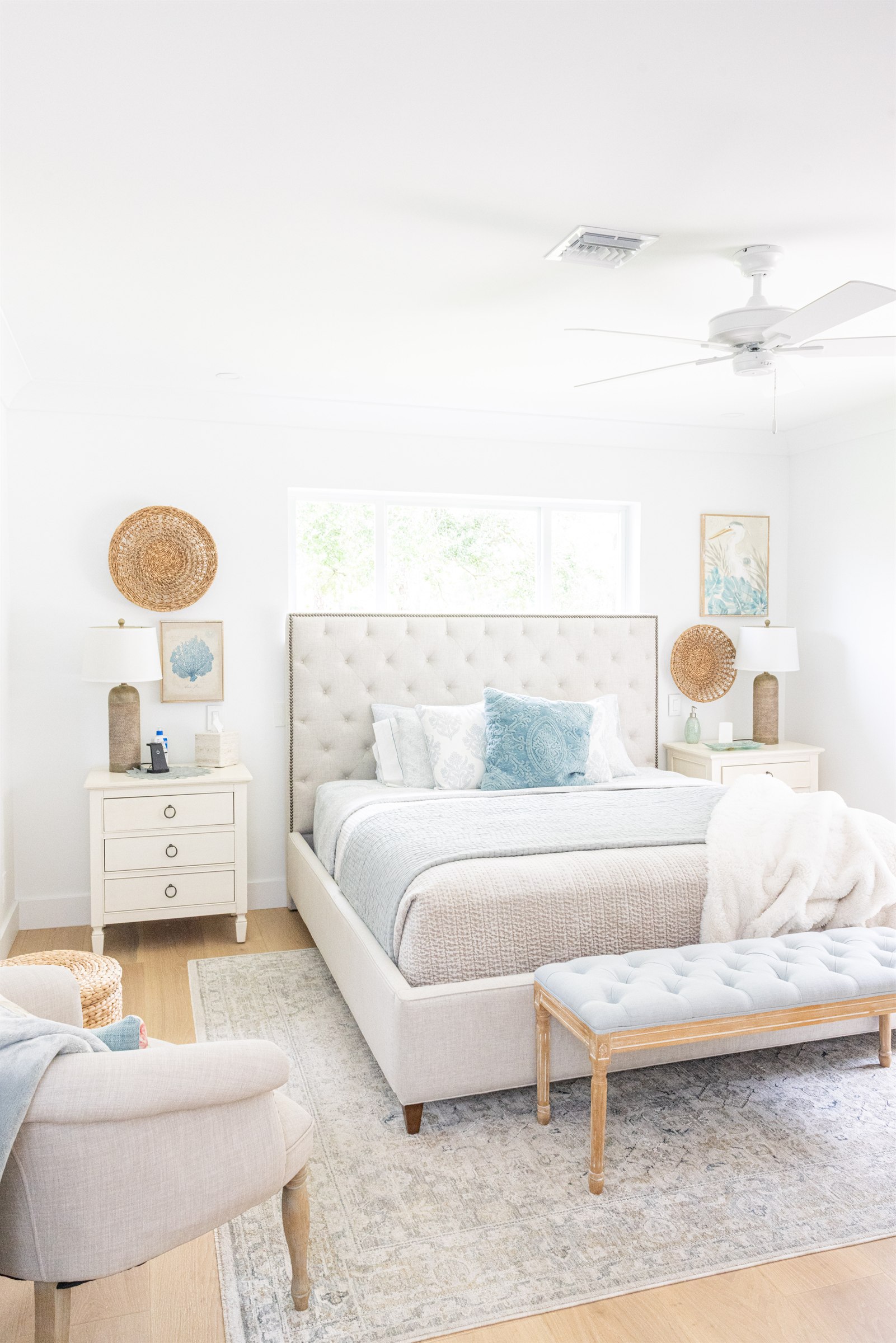 Master bedroom with tufted linen headboard, blue medallion pillow, and coastal heron art