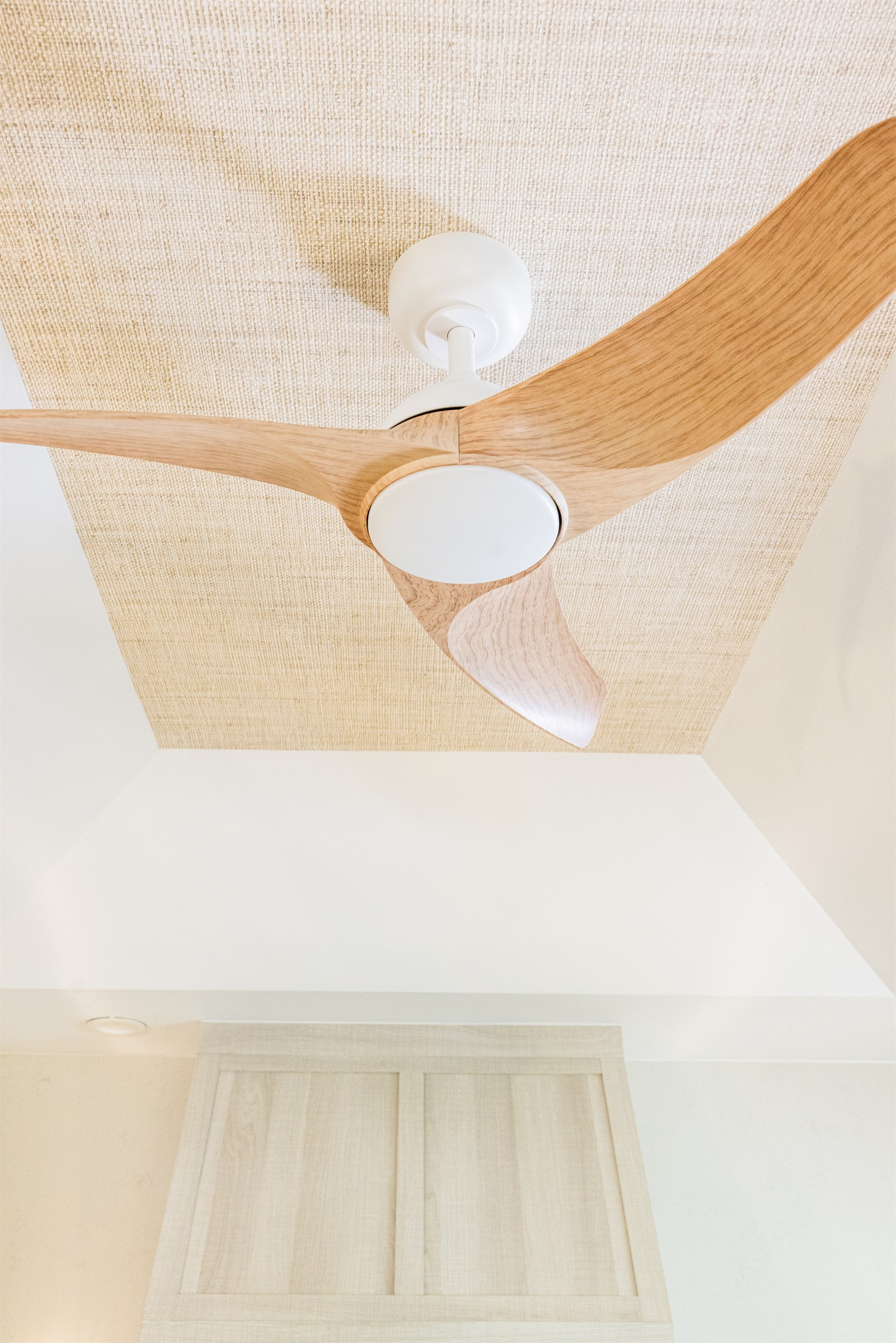 Detail of a wood-blade ceiling fan against a woven raffia ceiling