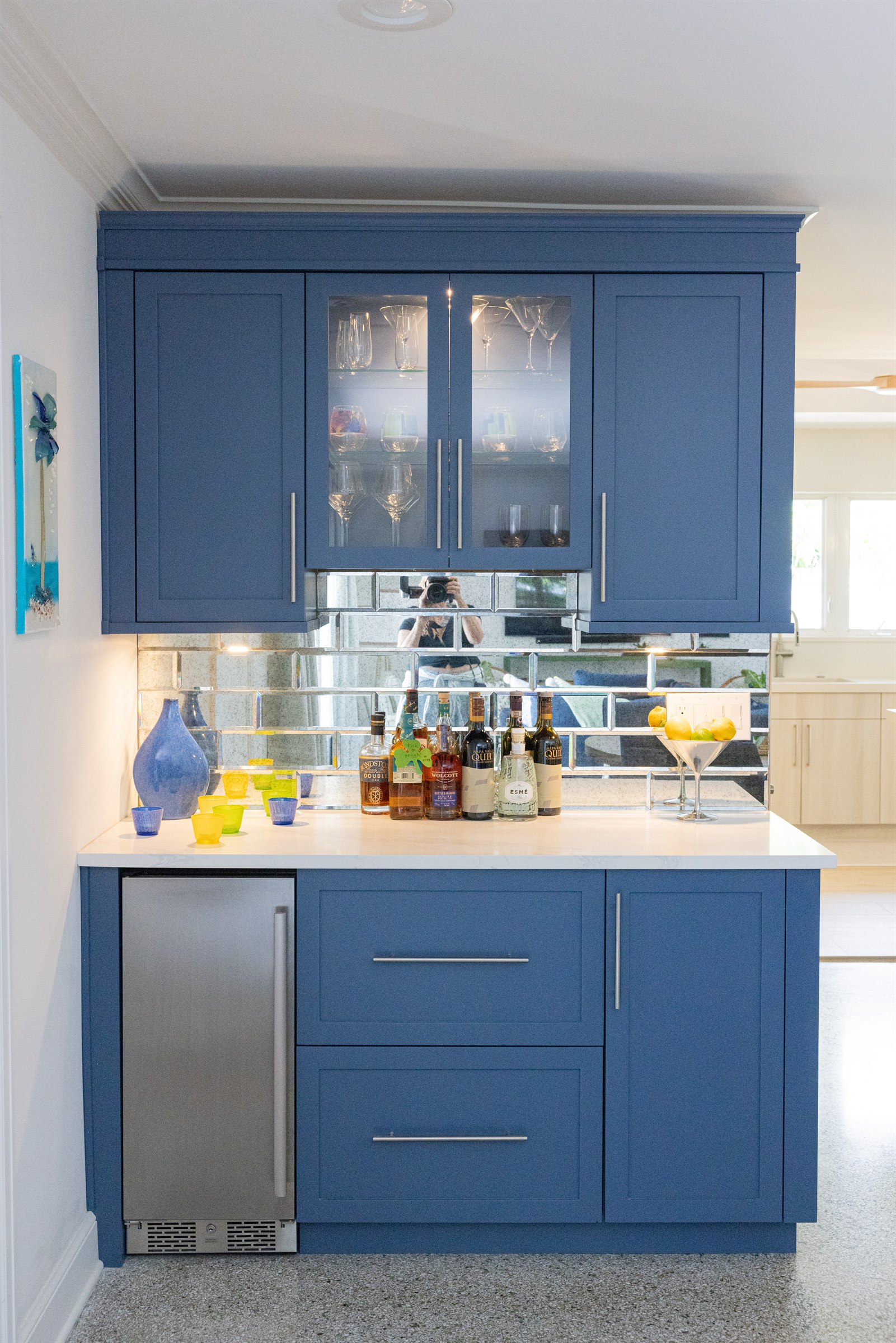 Navy blue bar cabinet with mirrored subway tile backsplash and colorful glassware