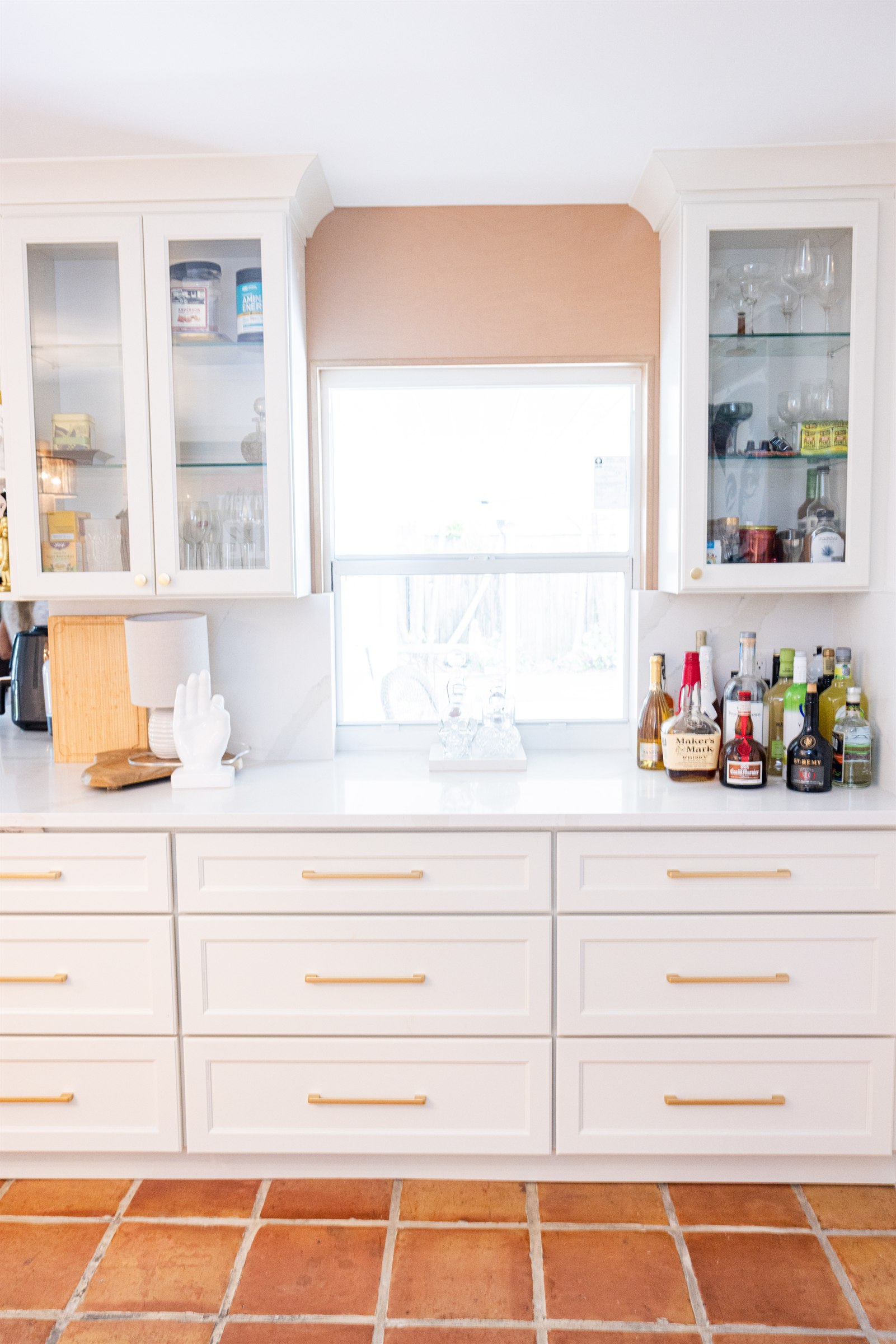 White cabinetry bar with terracotta tile floor, sunny window, and a whimsical hand-shaped lamp
