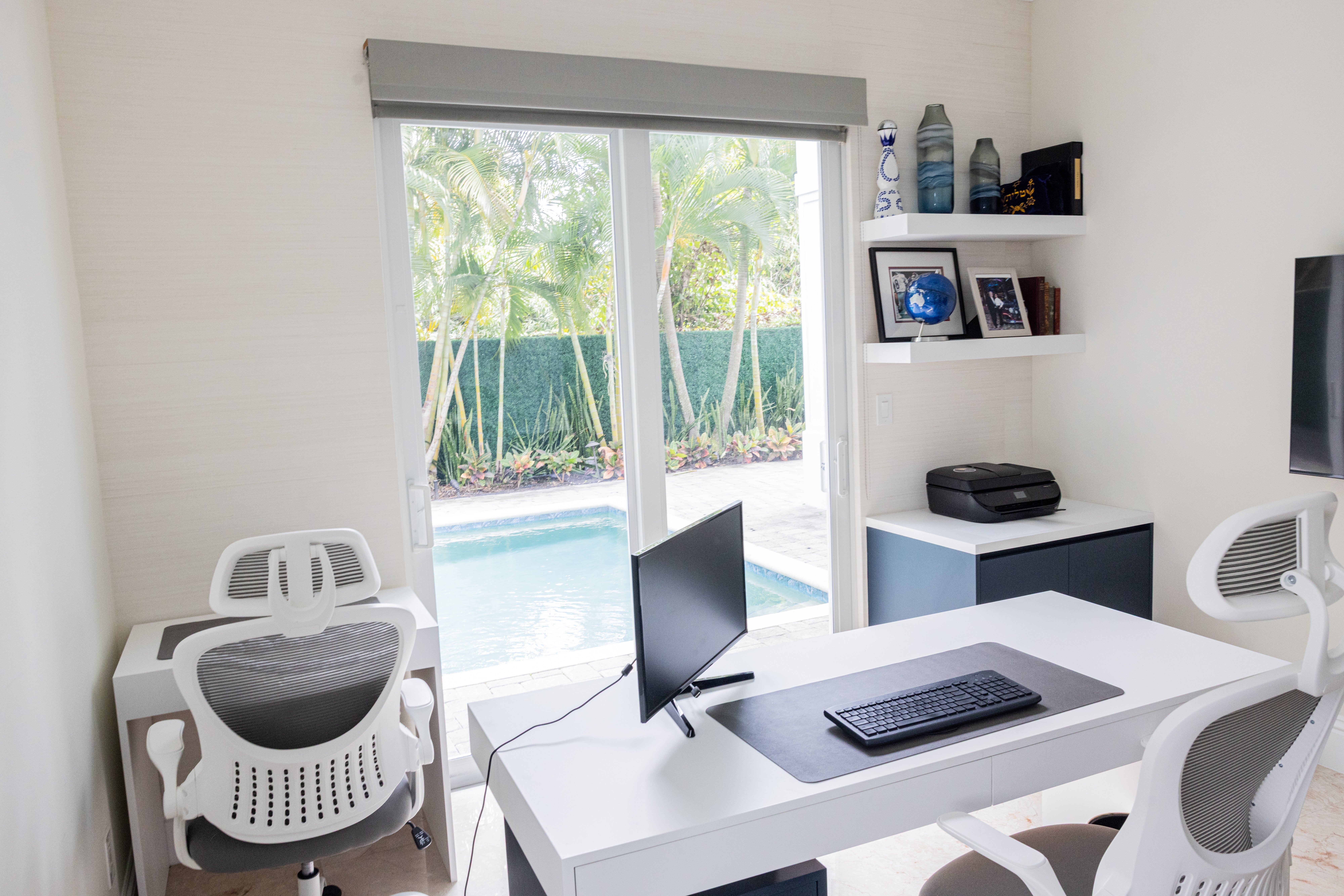 Home office with pool view, white desk and built-in shelving