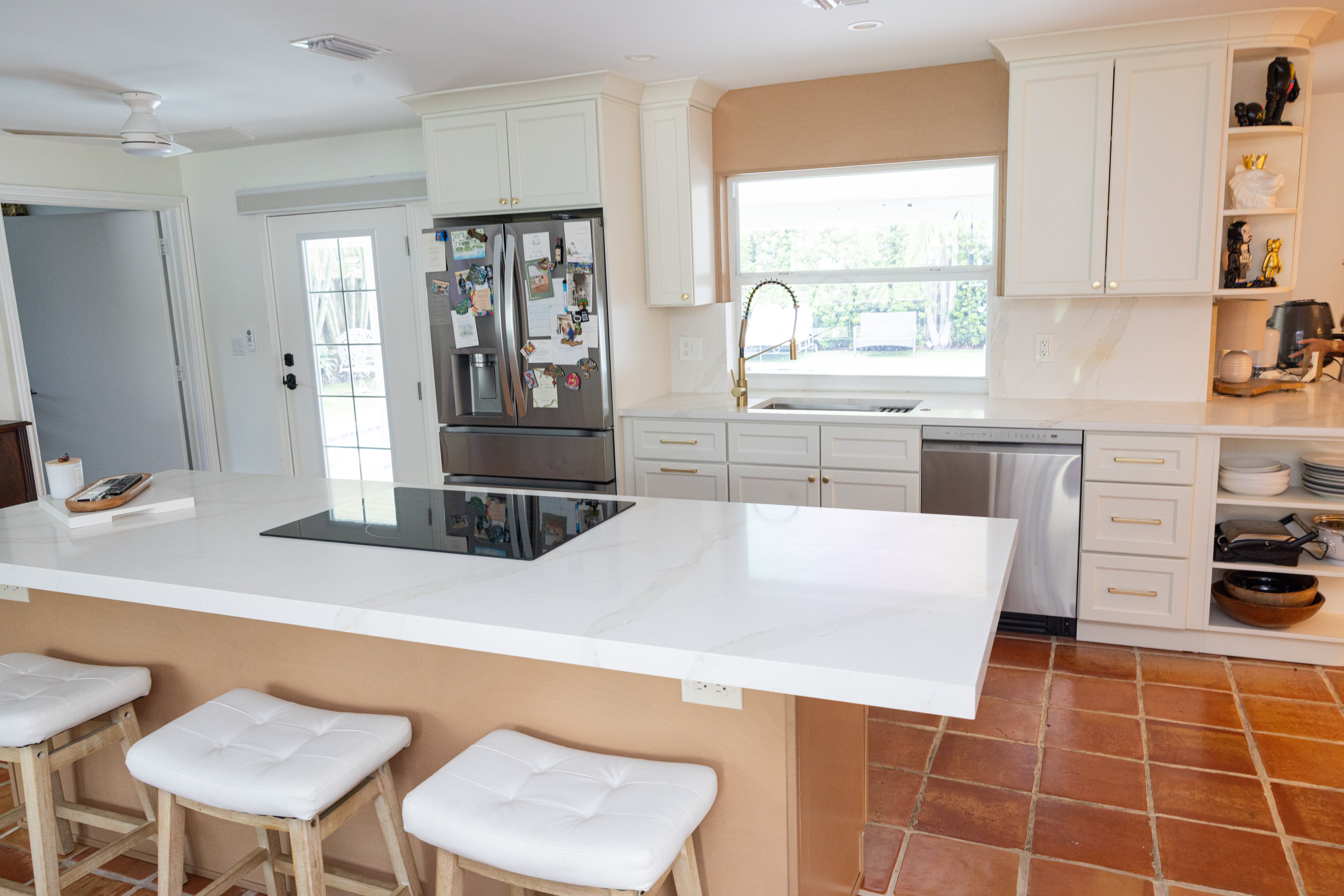 White kitchen with quartz island, induction cooktop and terracotta tile floor