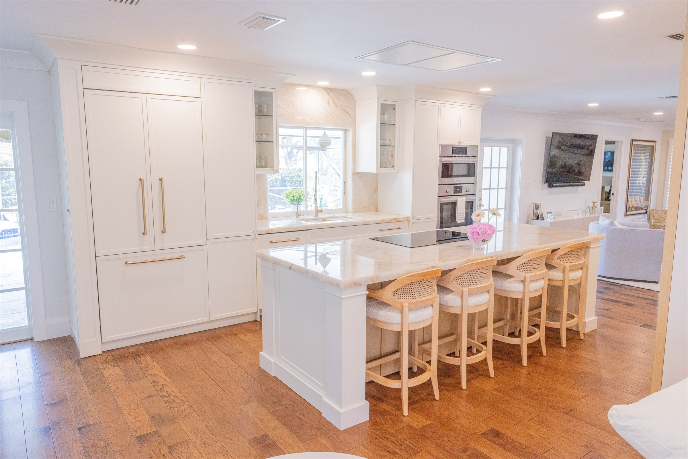 Bright white kitchen with large island, cane-back counter stools, and view to the family room
