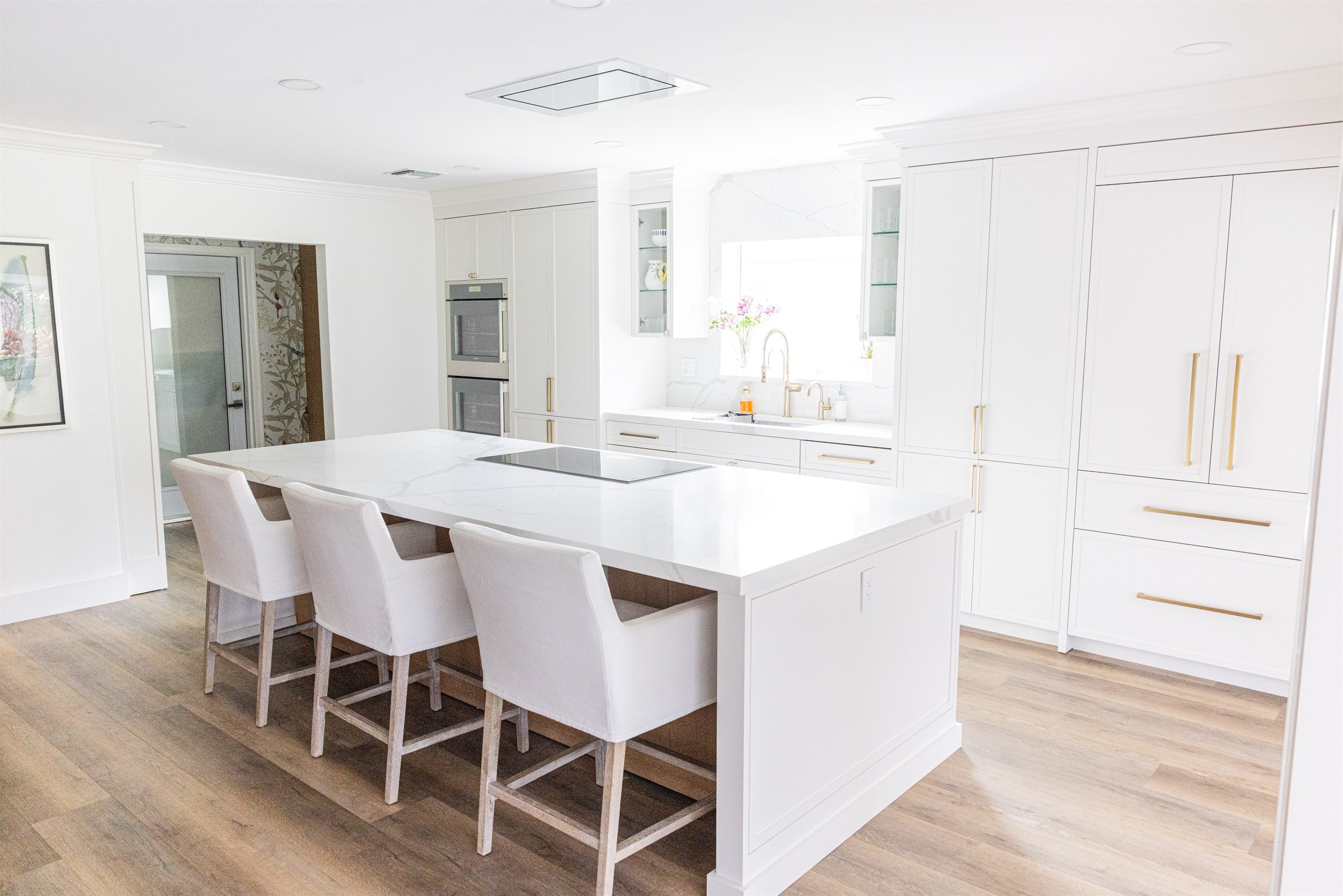 White kitchen island with three skirted counter stools and brass hardware, wide view