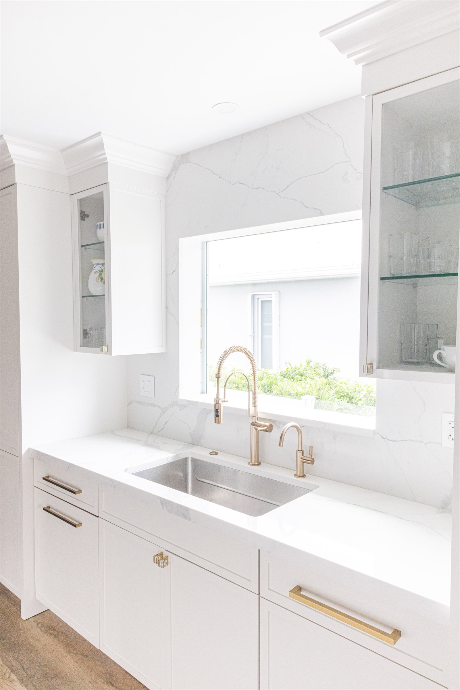 White kitchen prep sink with brass gooseneck faucet beneath a marble backsplash