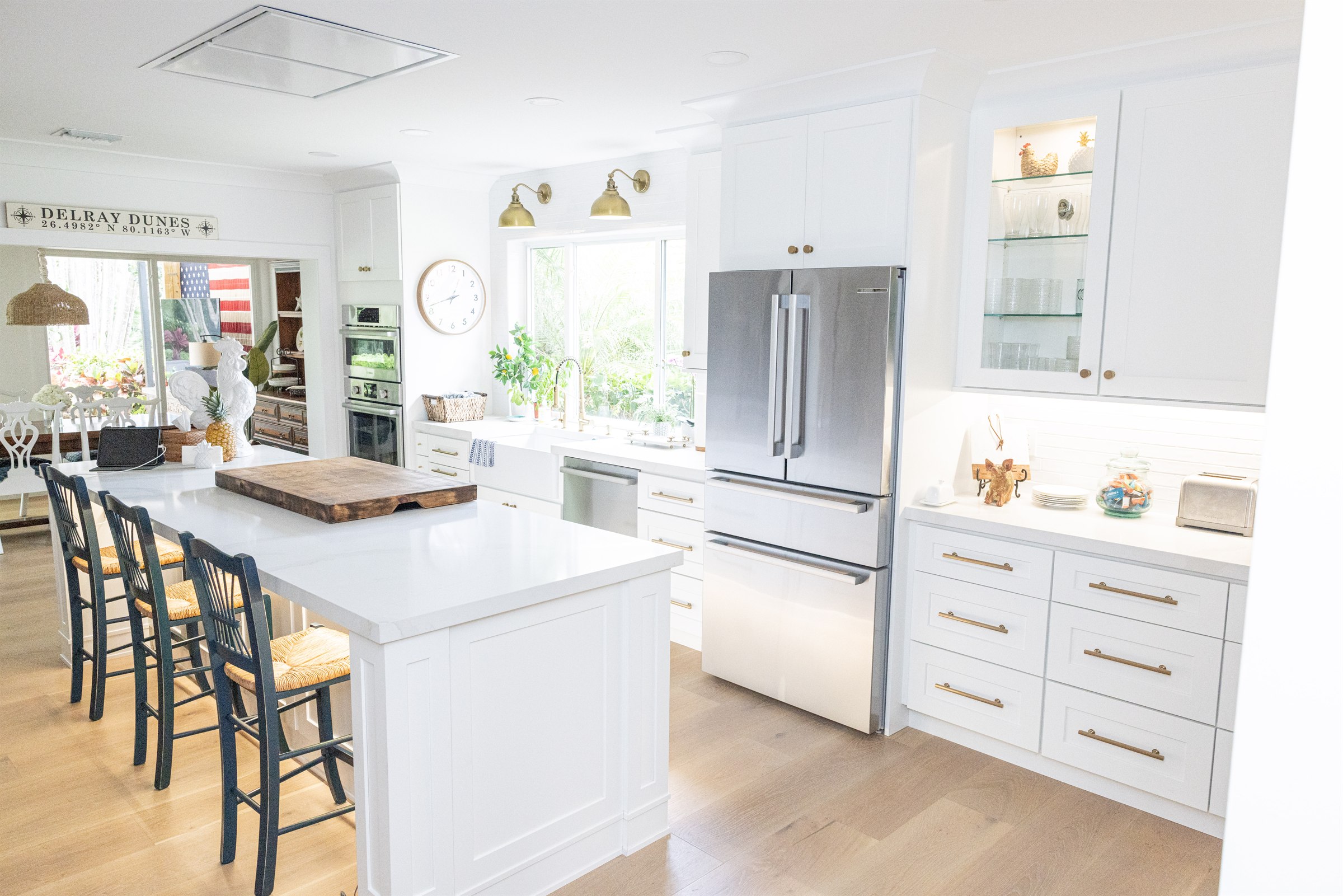 White kitchen with Delray Dunes sign, navy rush-seat chairs, and glass cabinetry