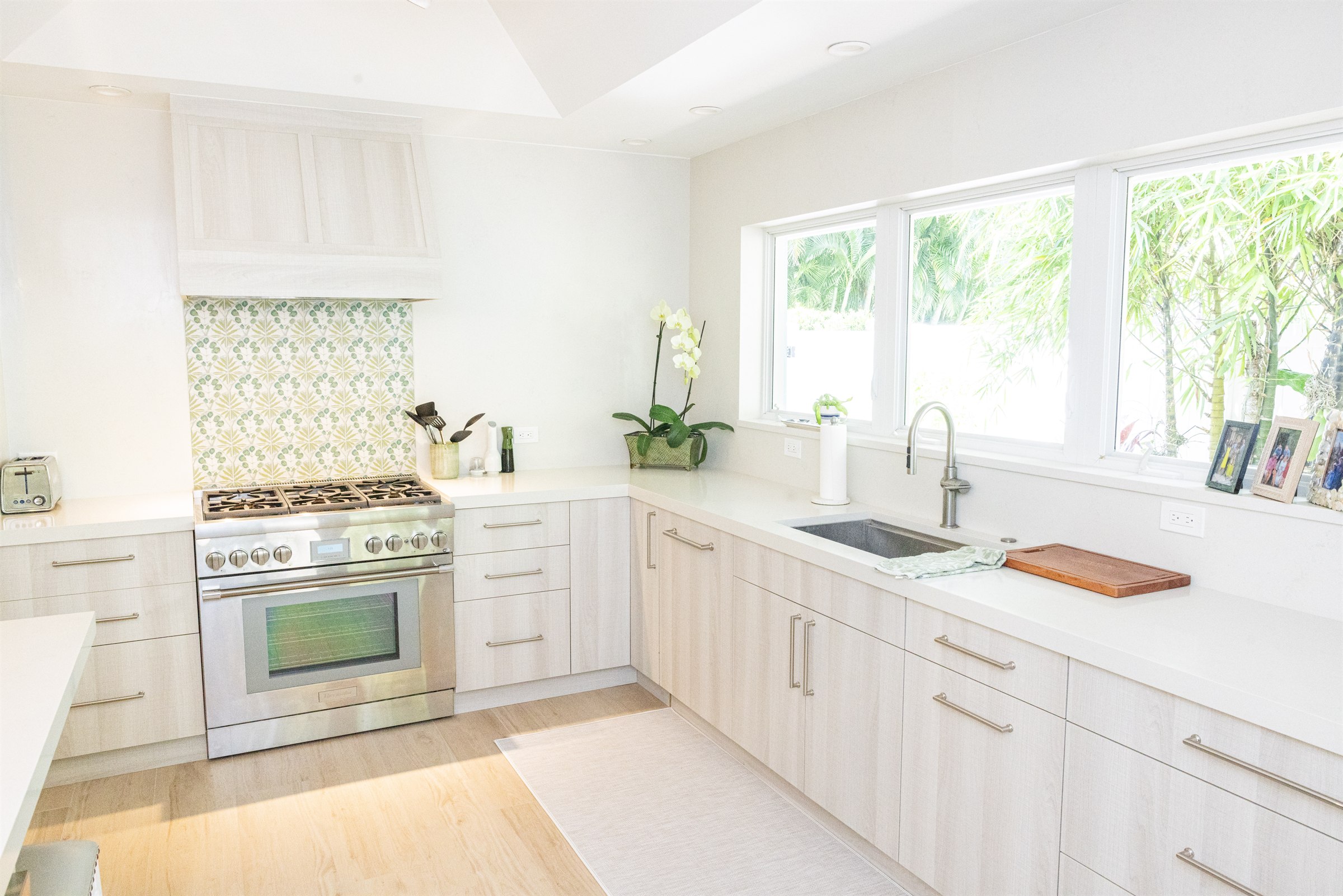 Light wood kitchen with green floral tile backsplash and stainless range, wide view