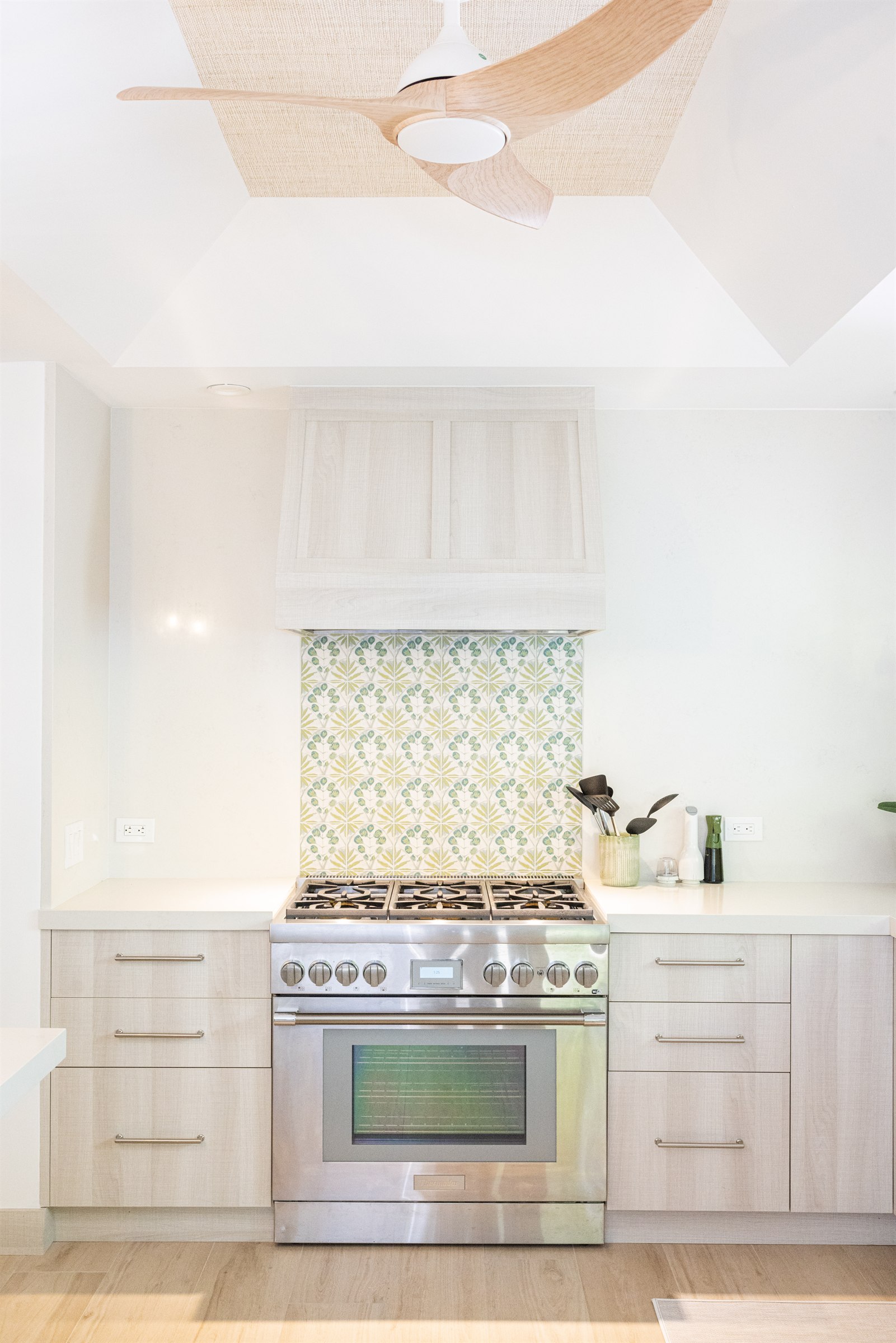Close view of the range hood and ceiling fan above the green floral tile backsplash