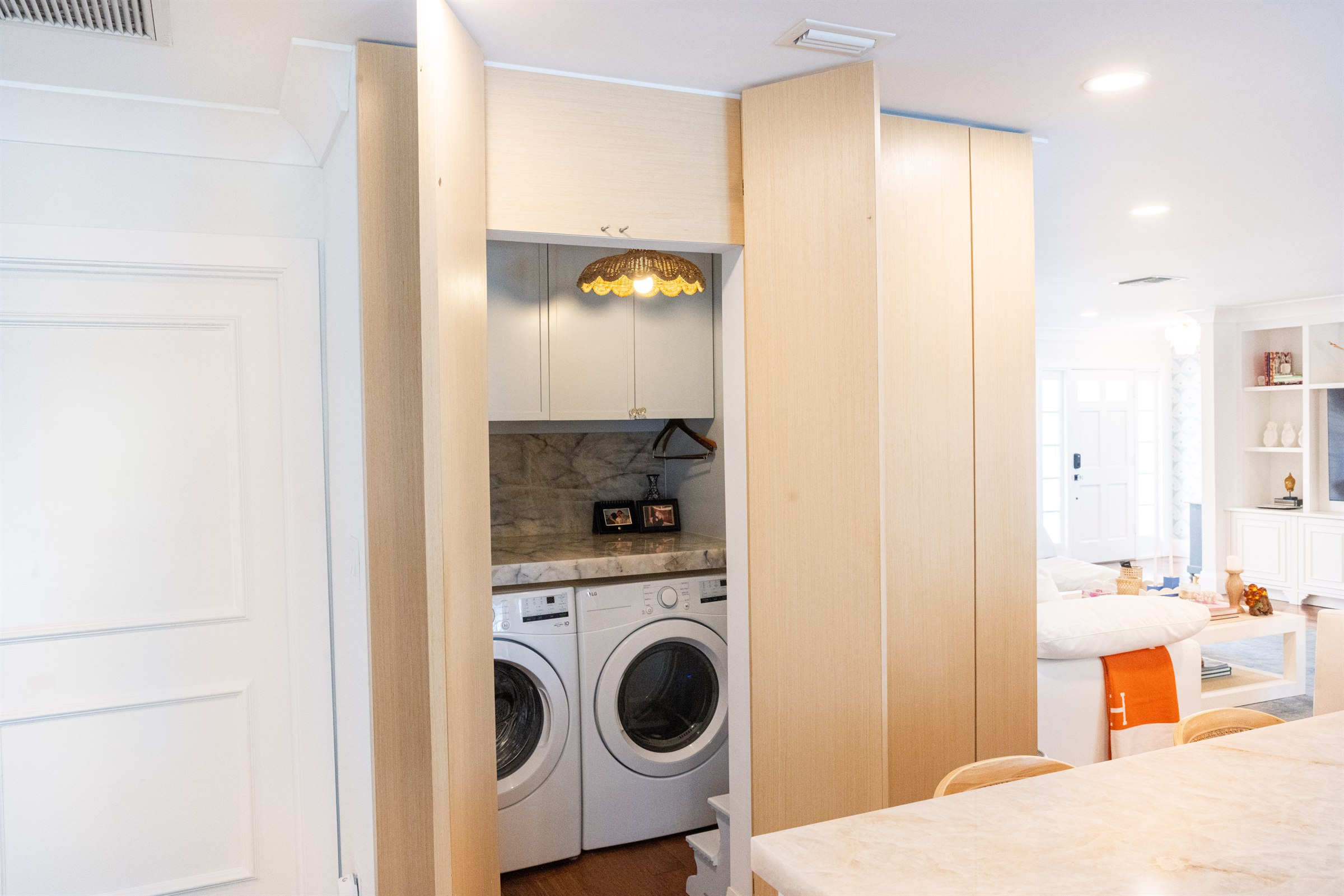 Built-in laundry nook with light oak cabinetry, marble backsplash, and a woven pendant light