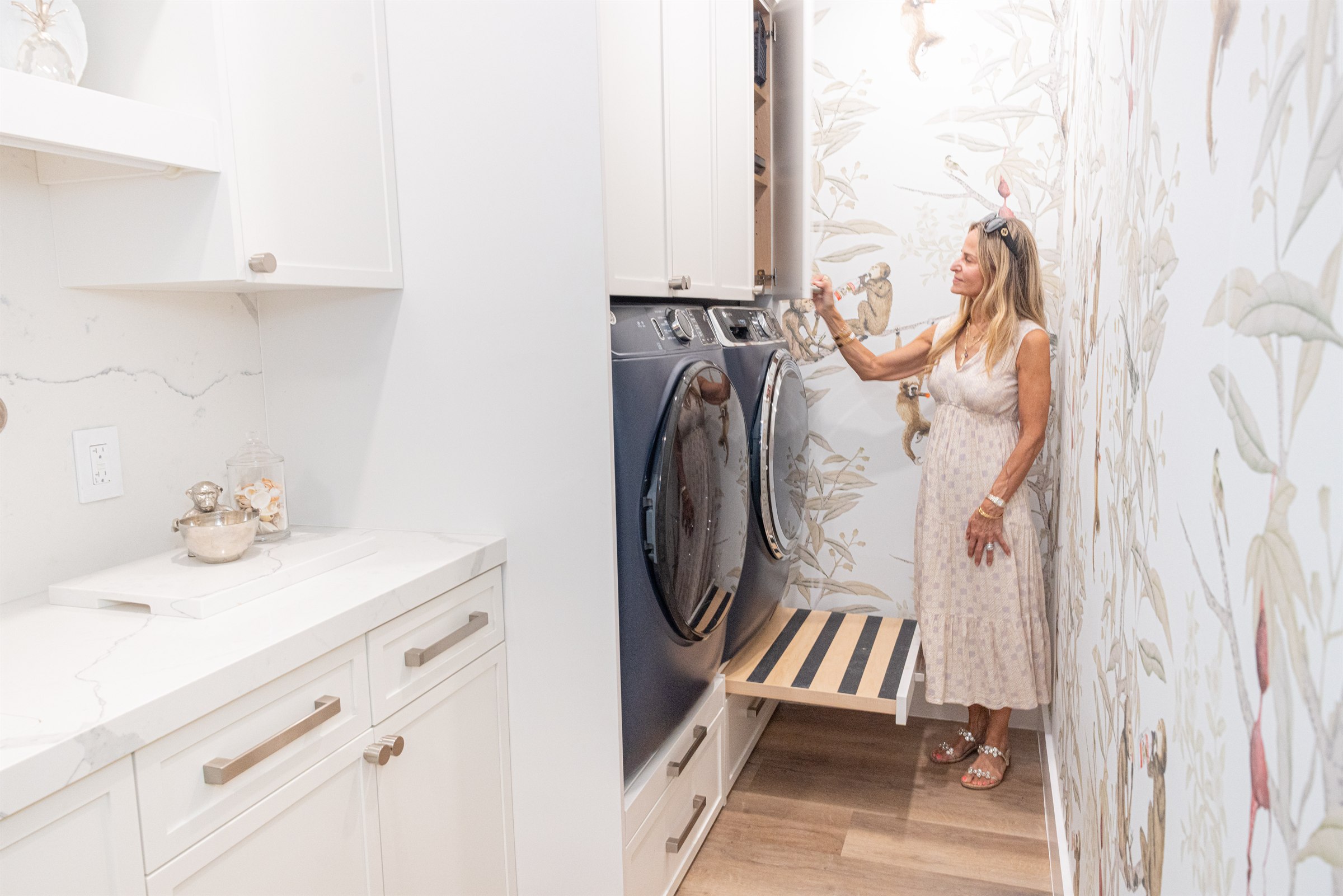 Designer styling a shelf beside navy Electrolux washer and dryer, playful monkey wallpaper
