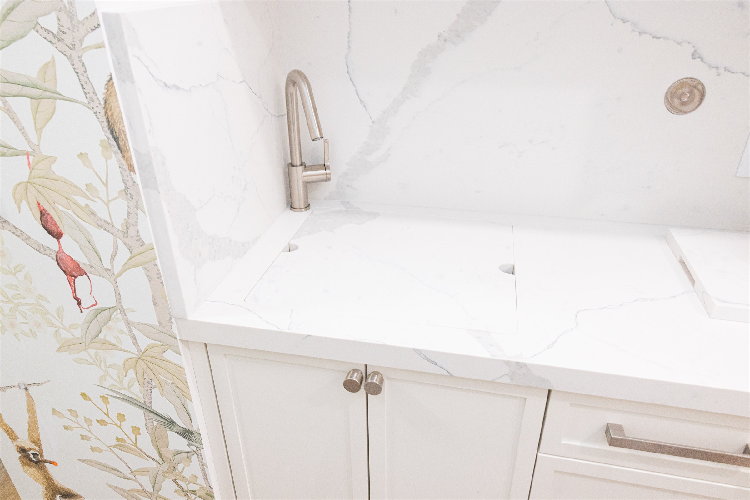 Marble backsplash and brushed nickel faucet detail above a quartz laundry counter