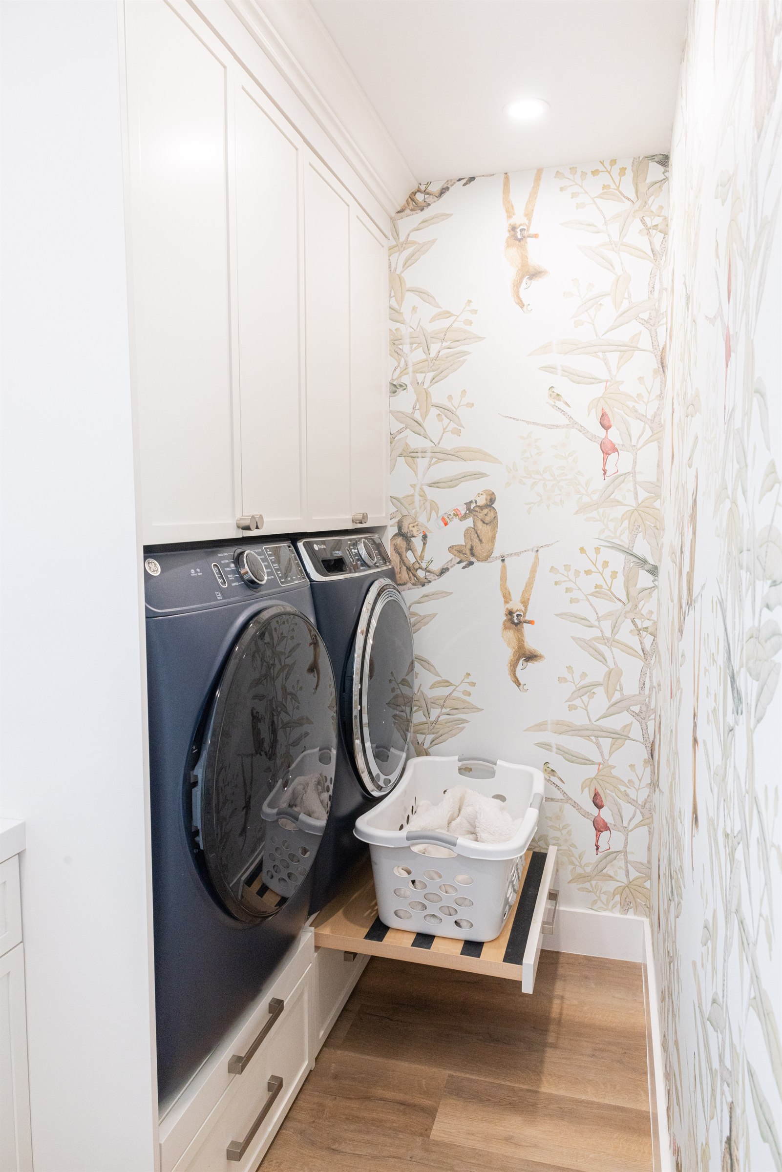 Navy Electrolux washer and dryer beneath whimsical monkey wallpaper with a pull-out laundry basket shelf
