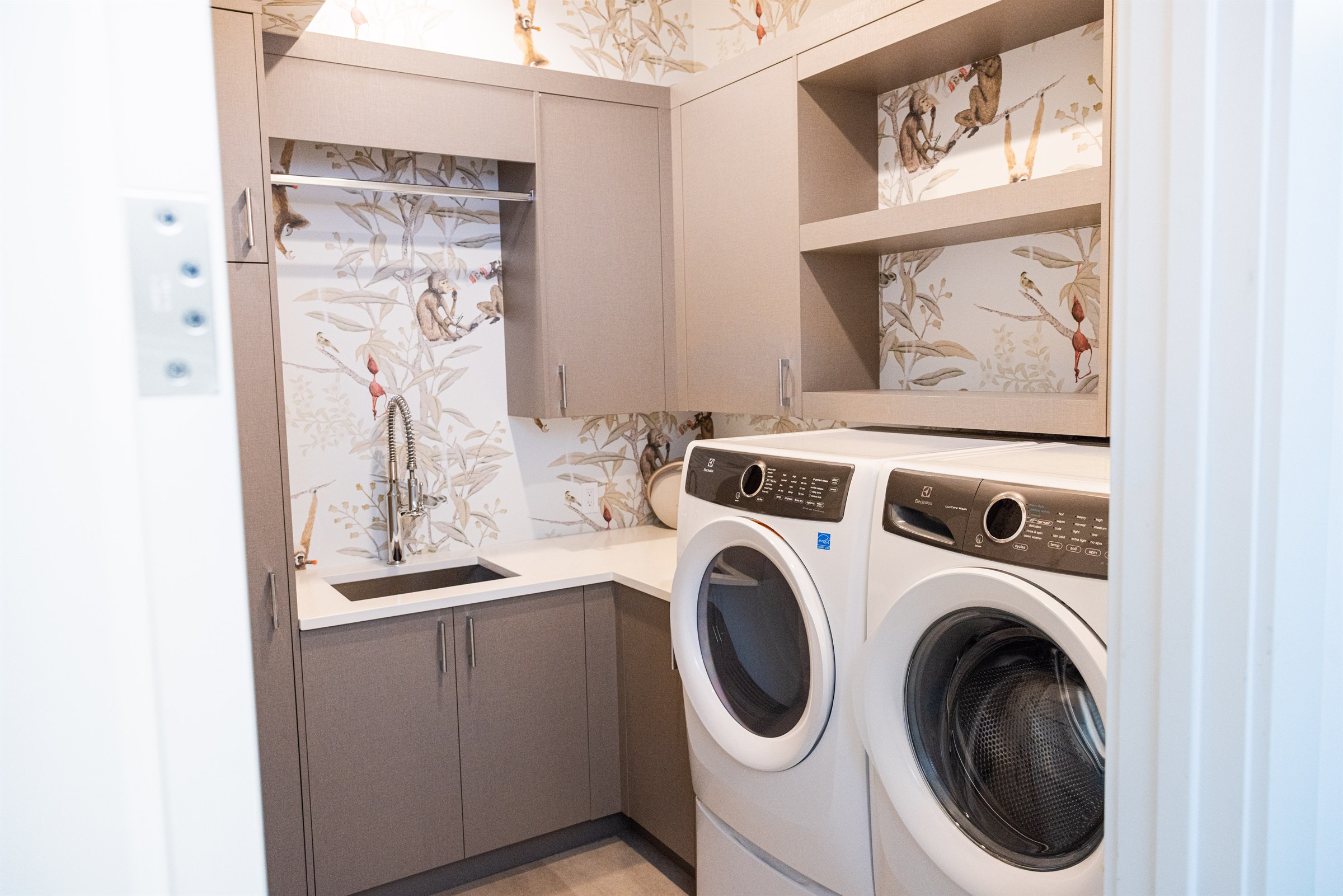 Taupe cabinetry laundry room with wildlife wallpaper and Electrolux washer and dryer