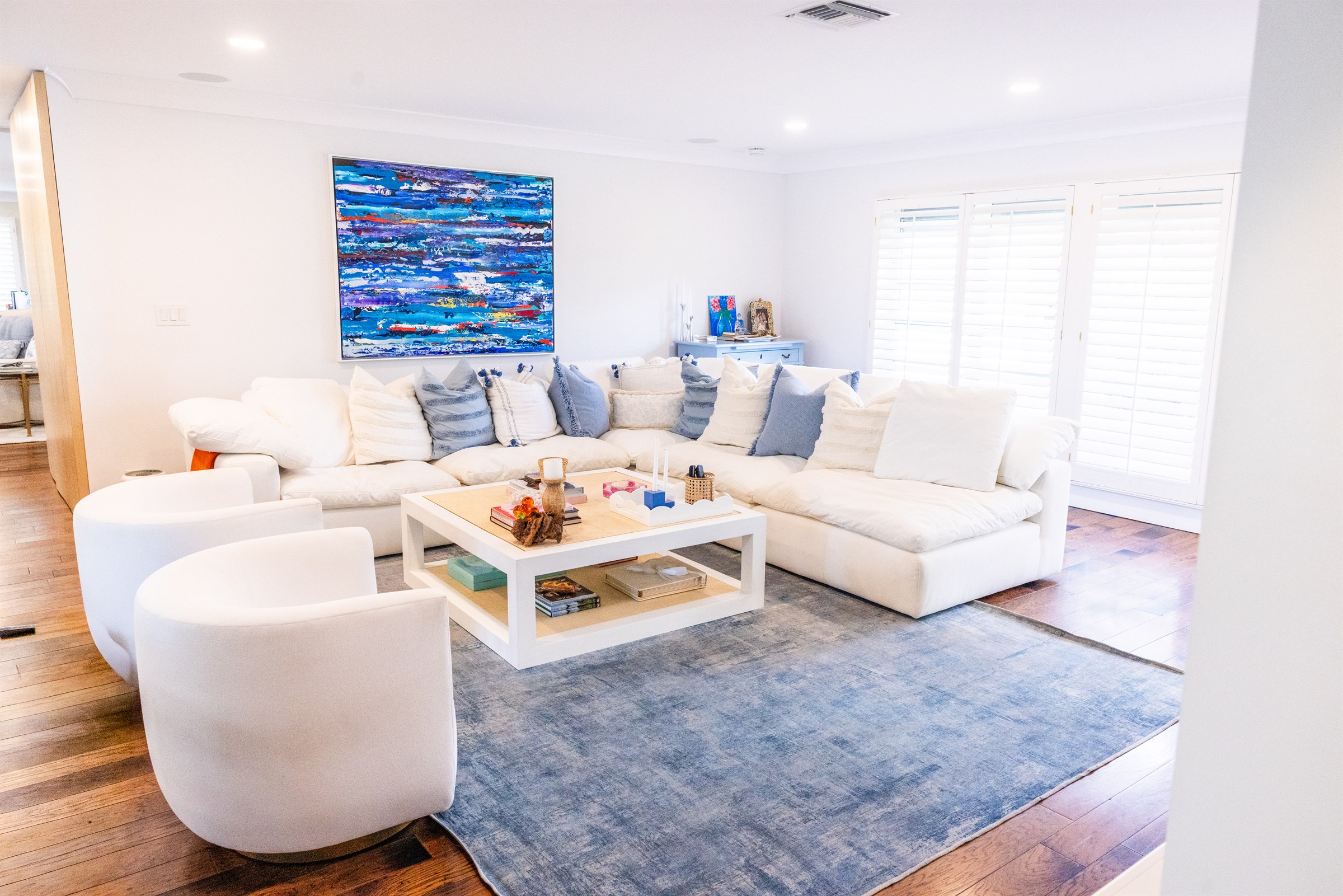 Bright living room with white sectional sofa, blue abstract artwork, and swivel accent chairs