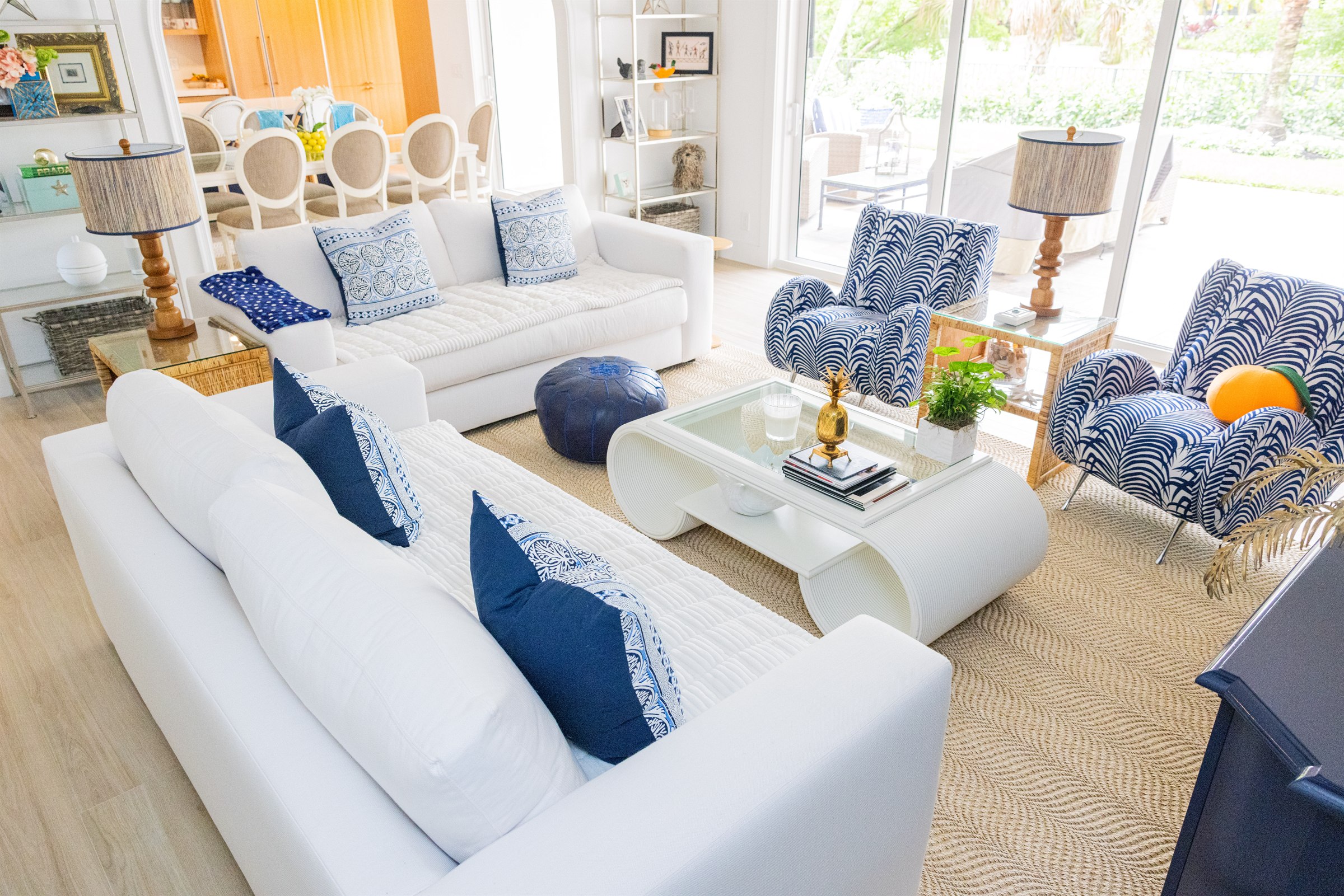 Coastal living room with white sofas, navy accents, and blue palm-print armchairs opening to the dining area
