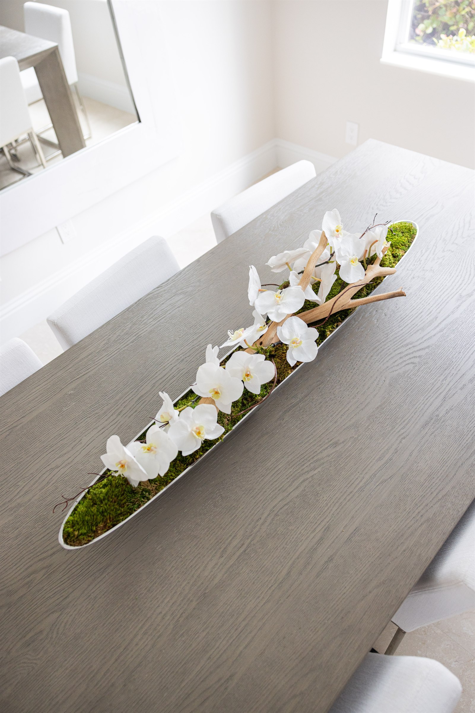 Dining table centerpiece of white orchids and driftwood on a bed of moss