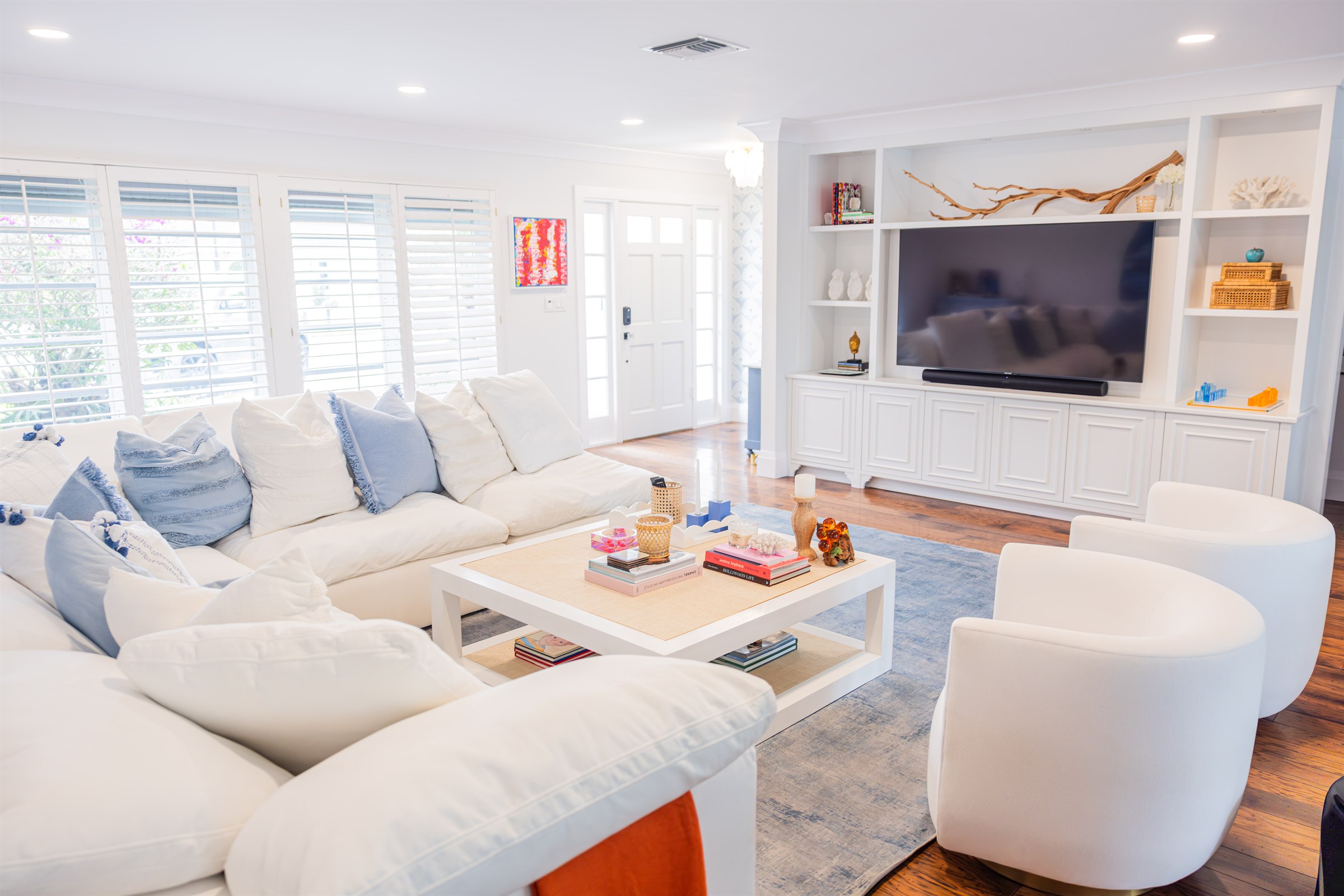 White sectional and swivel chairs facing a built-in entertainment wall with driftwood display