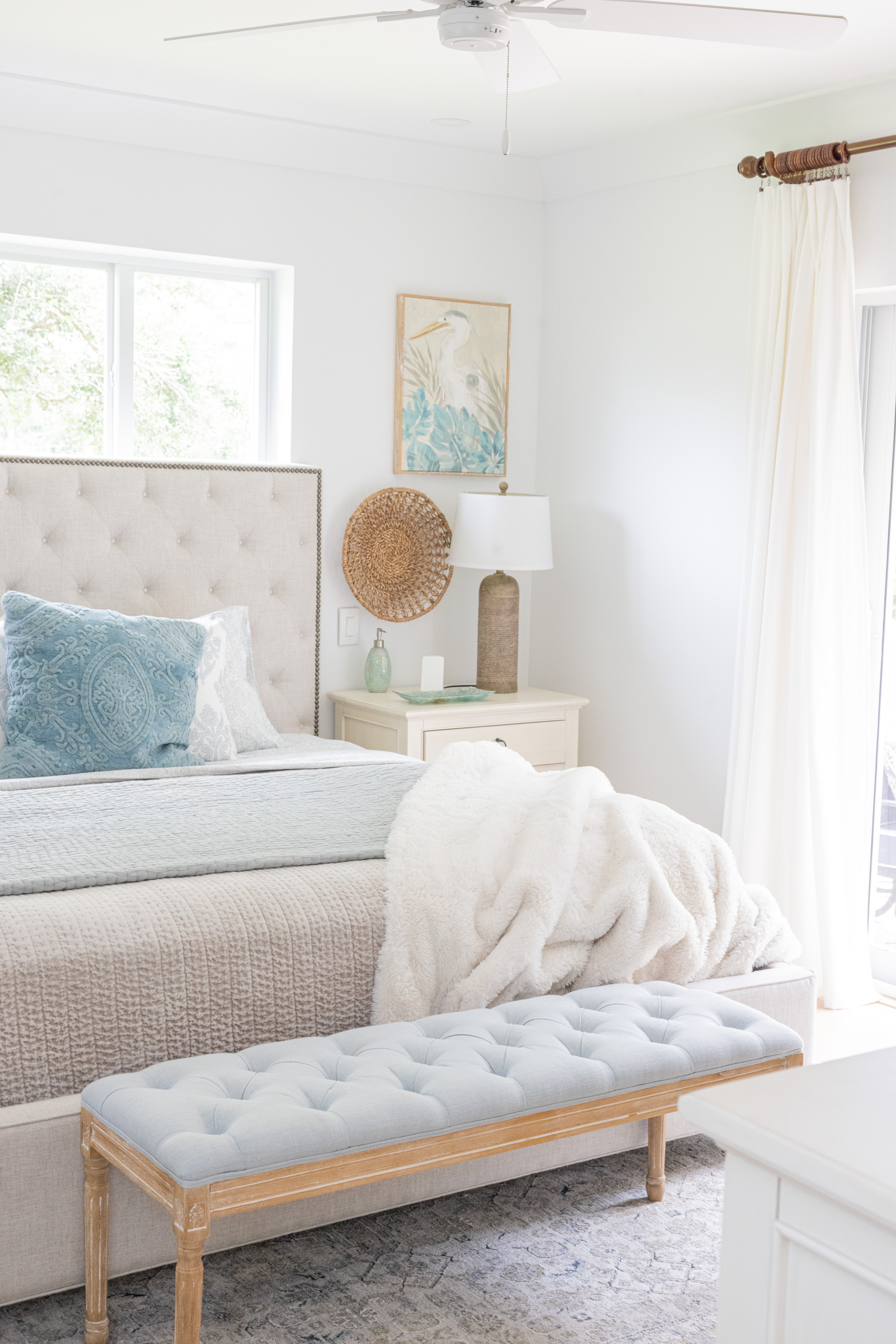 Master bedroom with tufted linen headboard, blue quilt and coastal heron art