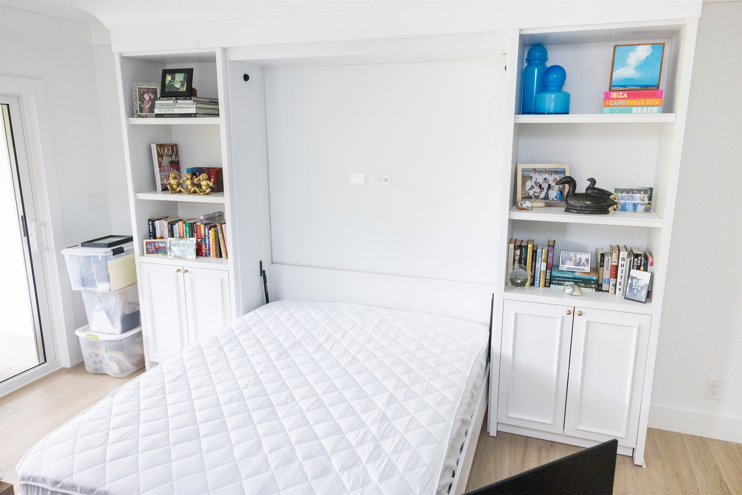 Murphy bed guest suite made up with quilted blue floral bedding and built-in display shelving