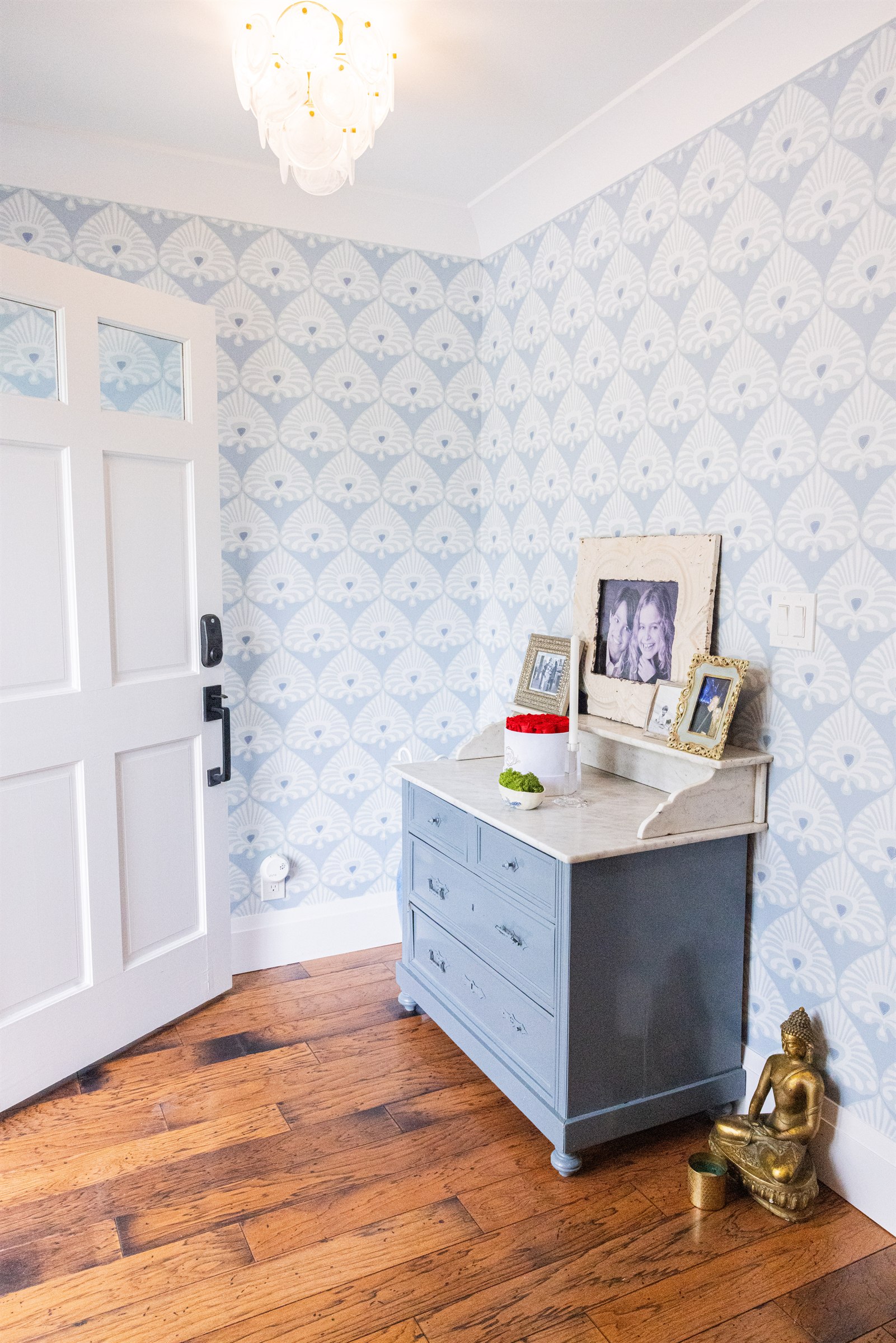 Entryway with scalloped blue wallpaper, antique blue dresser, and framed family photos