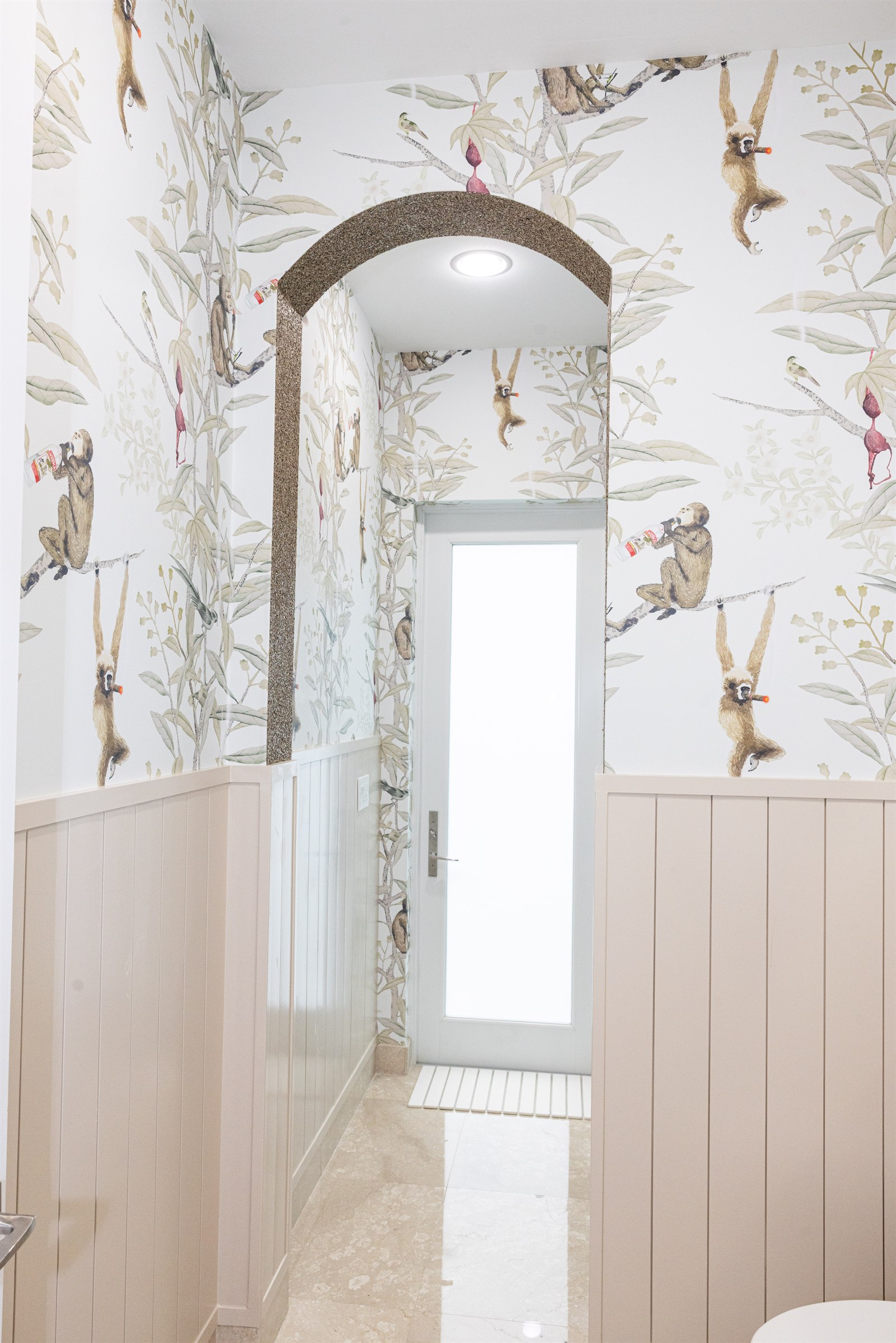 Powder room hallway with playful monkey wallpaper and a textured stone archway