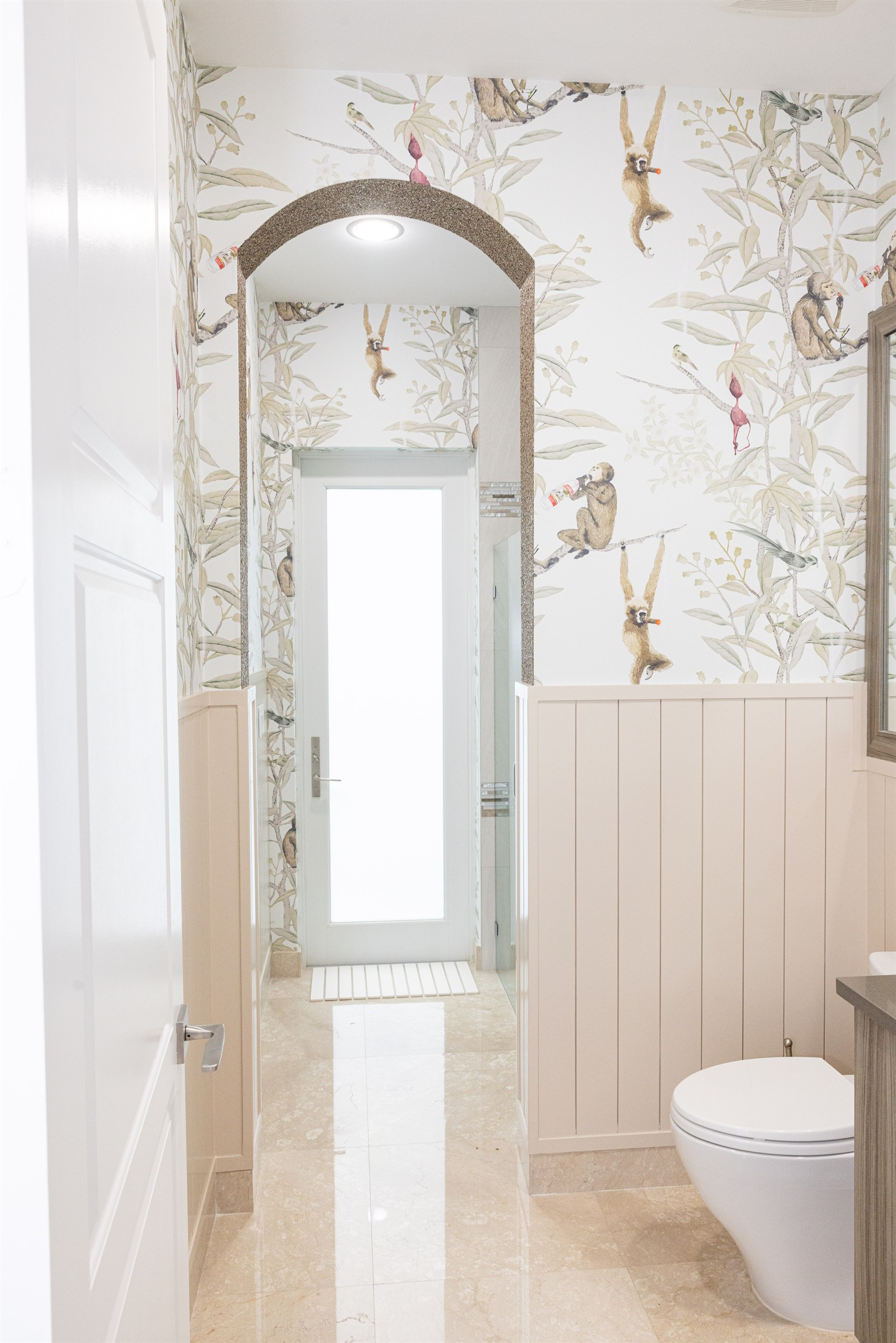 Powder room with monkey wallpaper, wainscoting, and a wall-mounted toilet