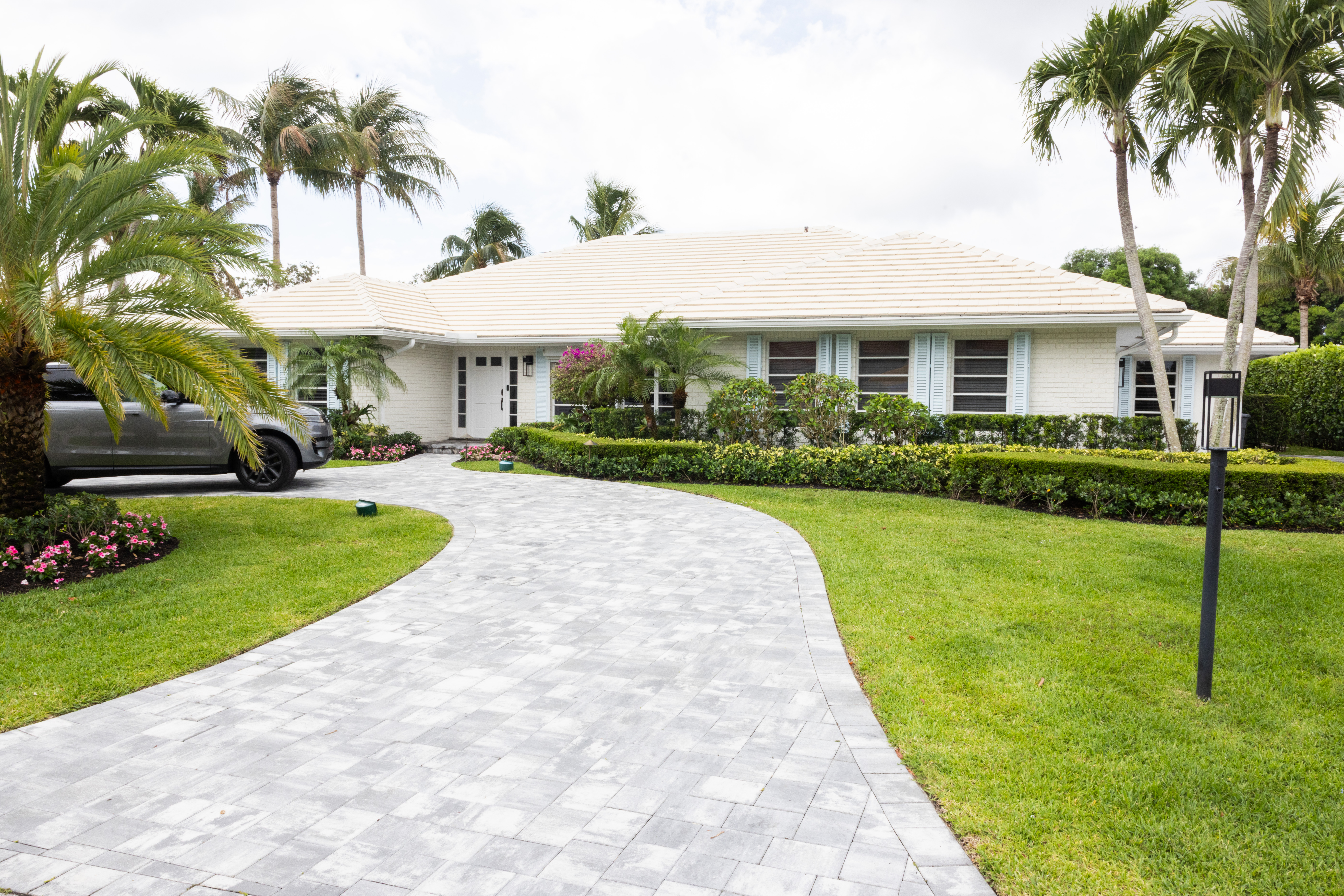 Curving paver driveway leading to white ranch home with teal shutters