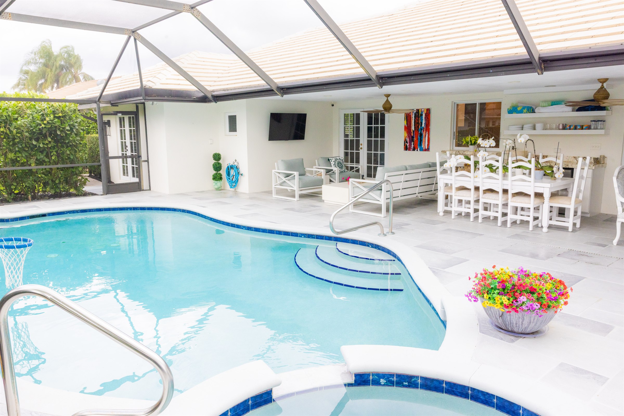 Screened pool patio with basketball hoop, blue-cushioned lounge seating, and a ten-seat dining table