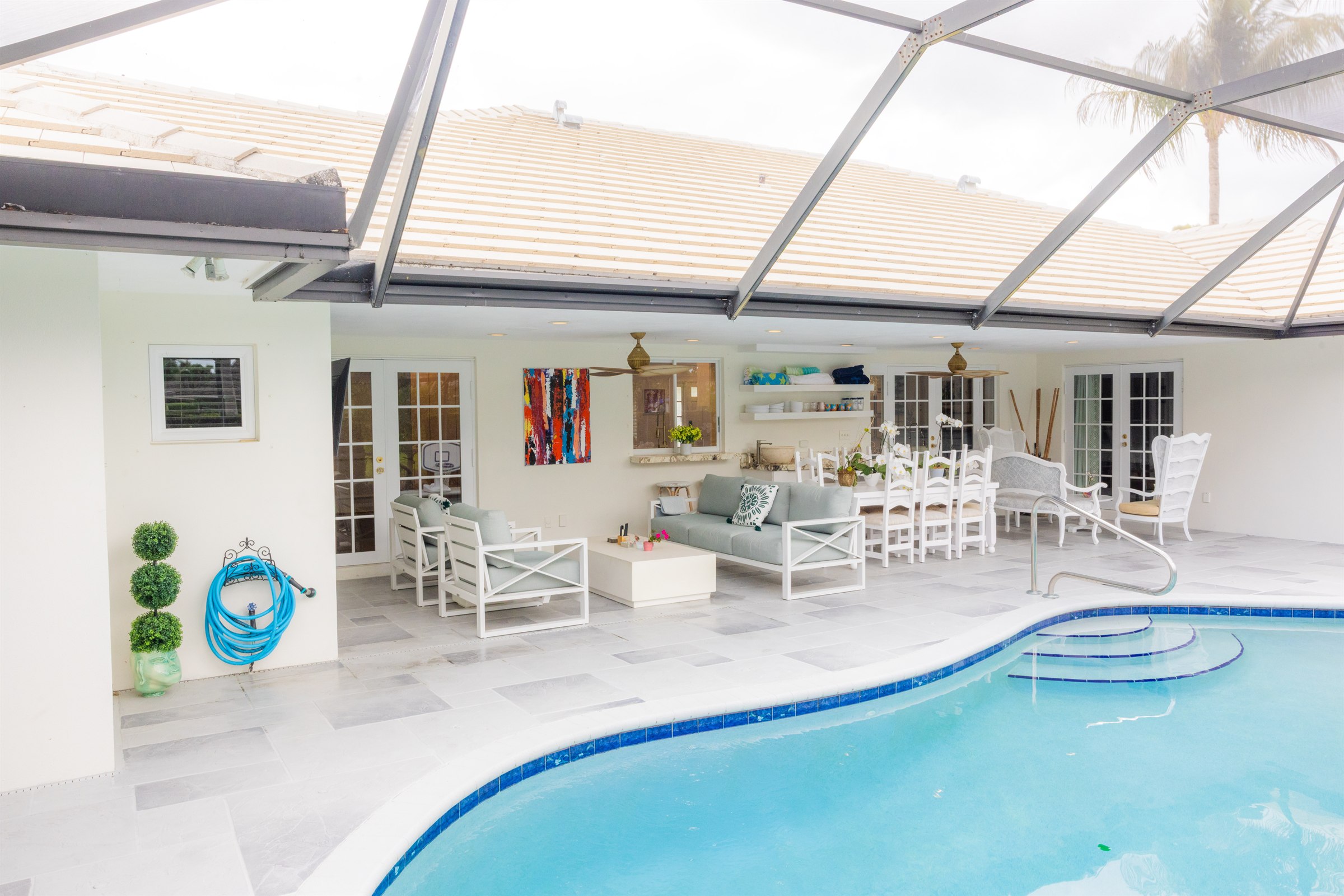 Covered lanai viewed from the pool, showing the full outdoor living room, dining table, and open wet bar shelving