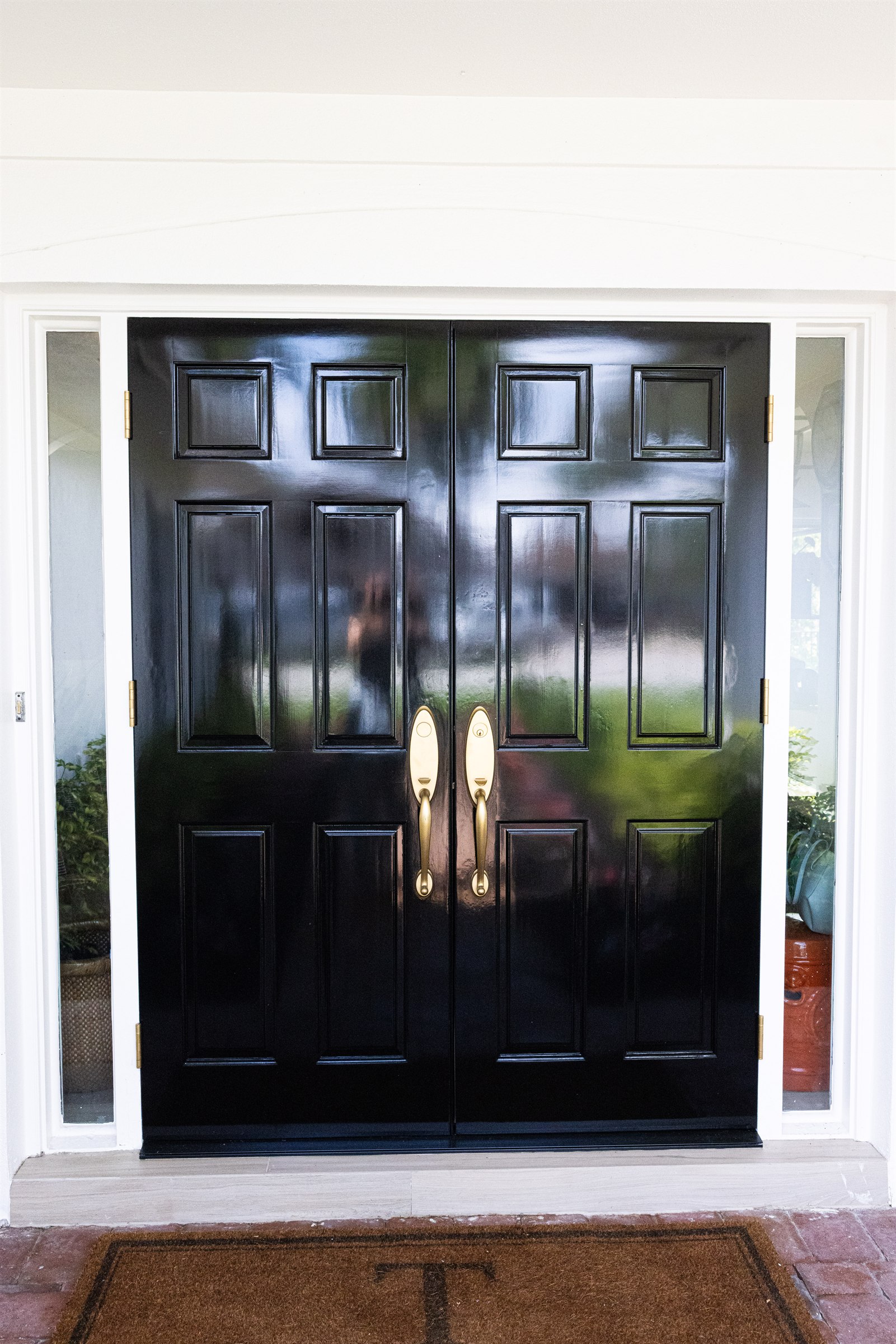 Glossy black double front doors with brass hardware and glass sidelights