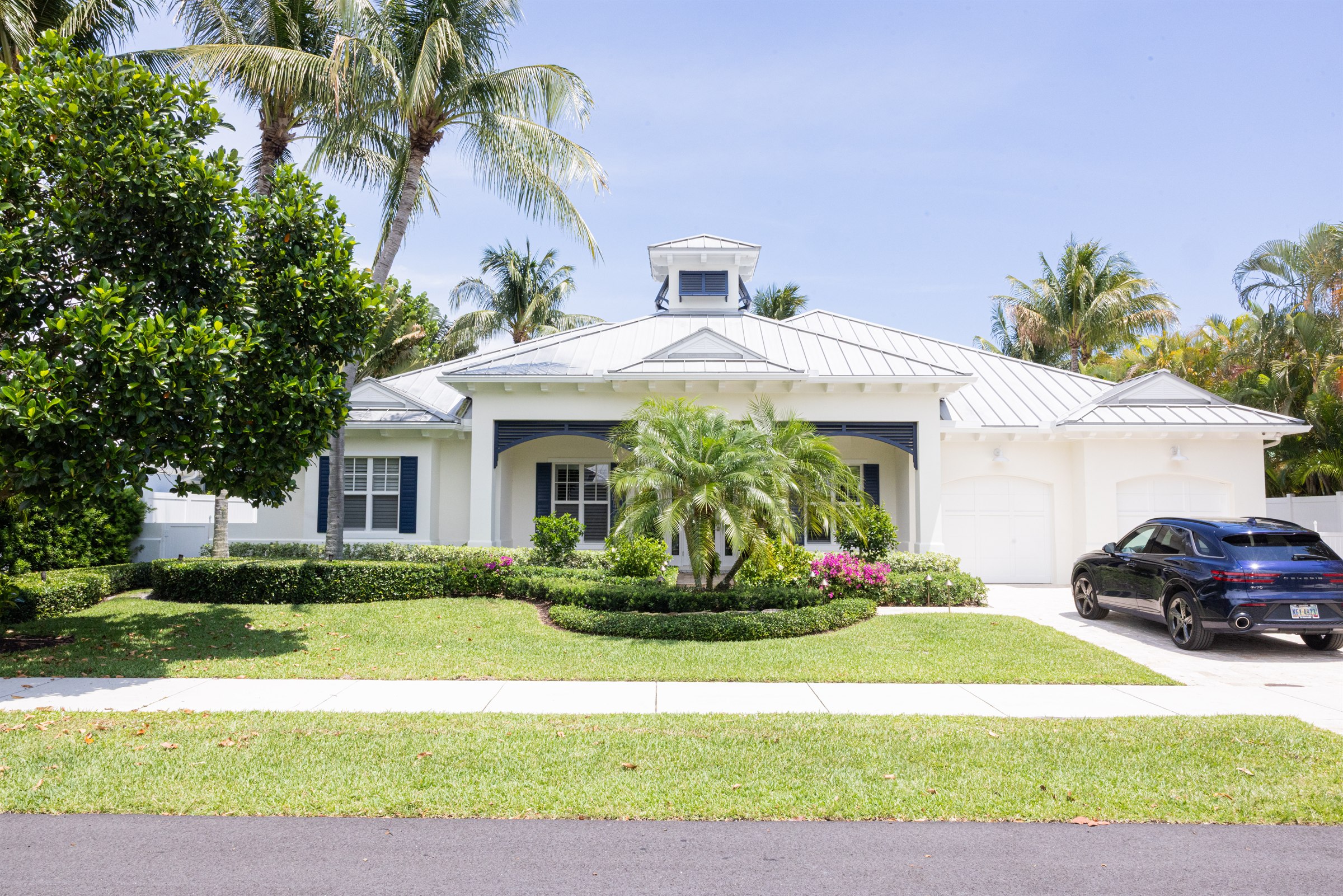 White coastal home with standing-seam metal roof, navy shutters, and a blue SUV in the driveway